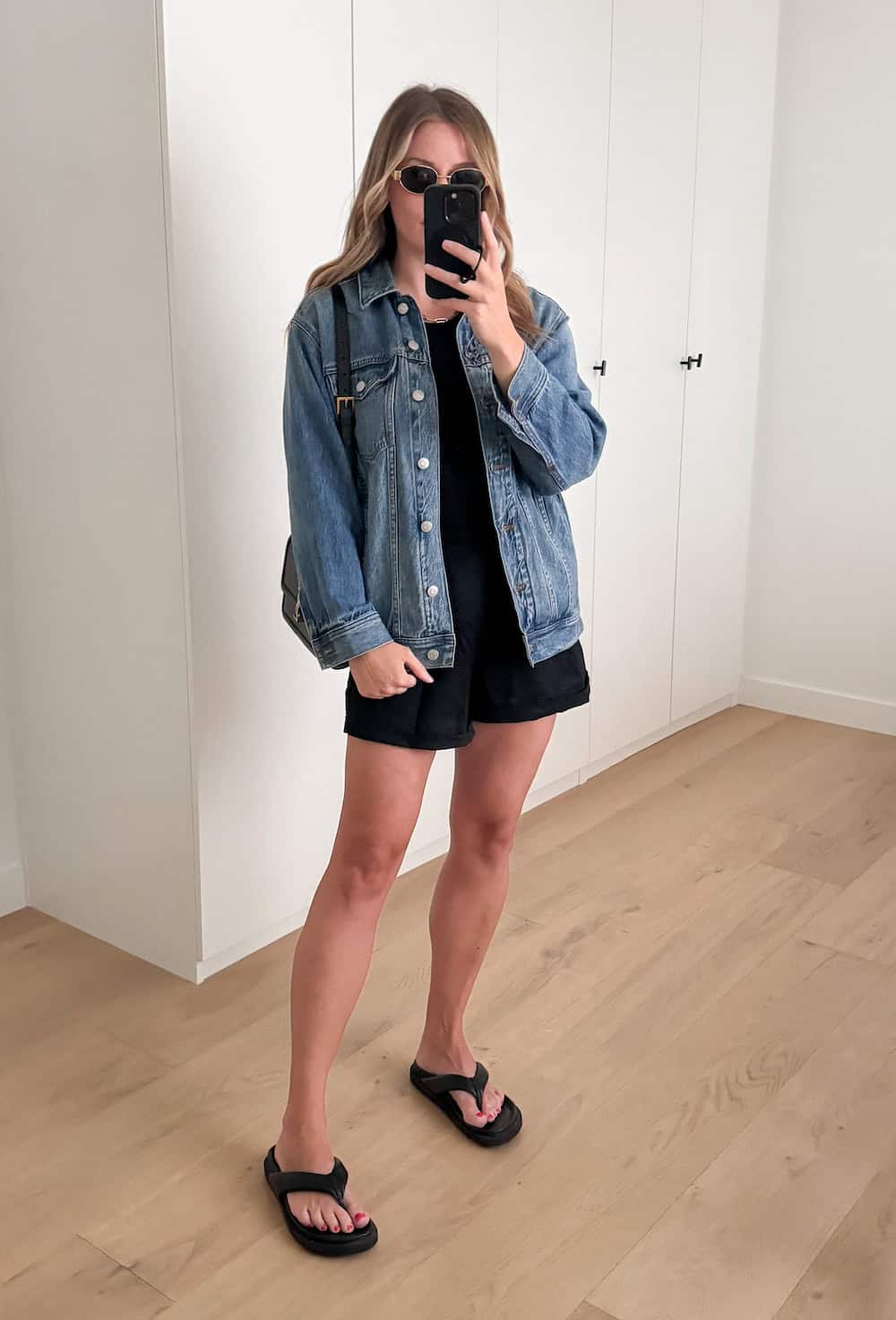 woman wearing a summer outfit with a denim jacket, black tank top, black linen shorts, and black chunky sandals