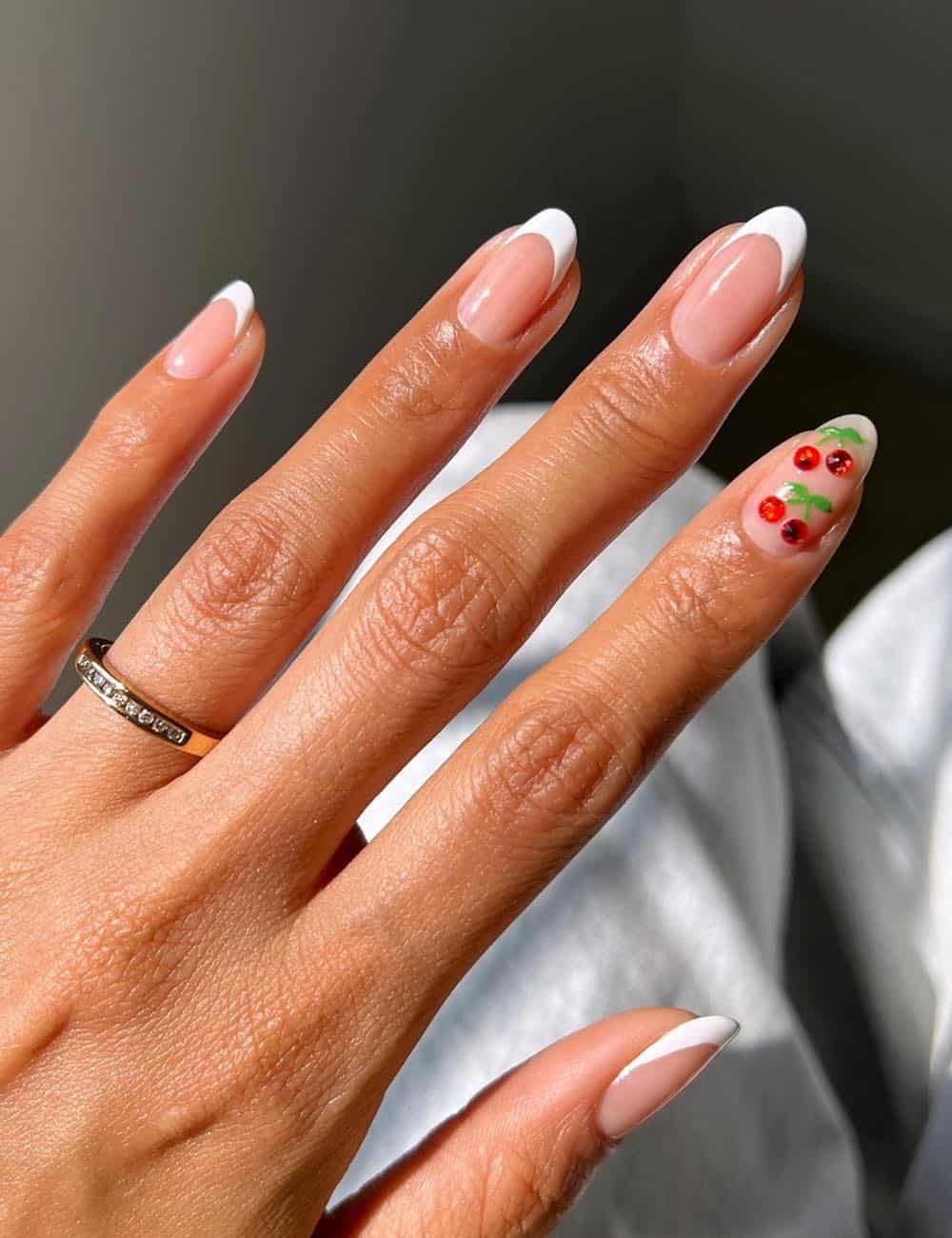 short round nude nails with white tips and an accent nail featuring cherry crystals