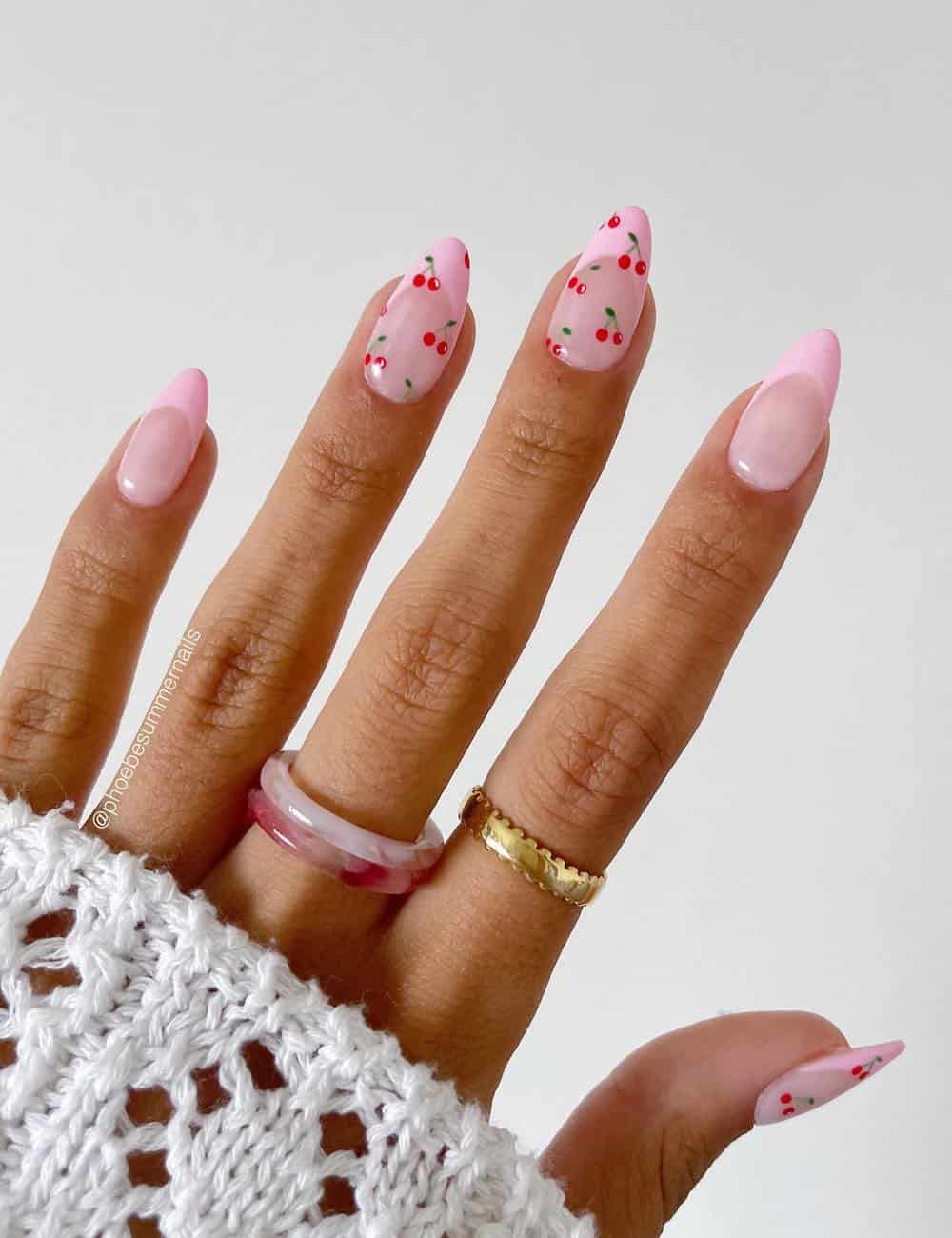 short nude pink almond nails with pink tips and two accent nails with cherry patterns