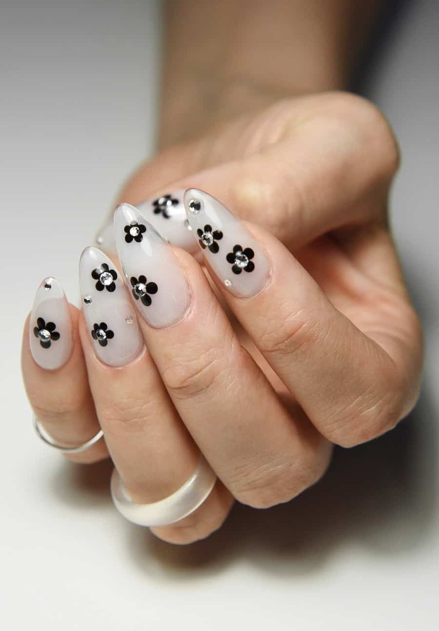 Long milky white almond nails with black floral art and gems