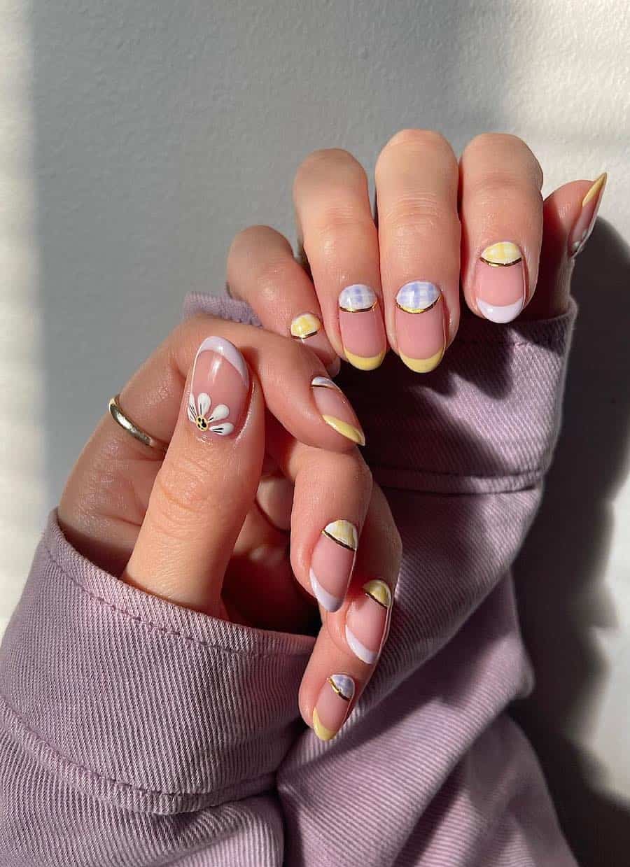 Short round nude nails with pastel yellow and purple French tips and half moons with plaid, floral, and gold details