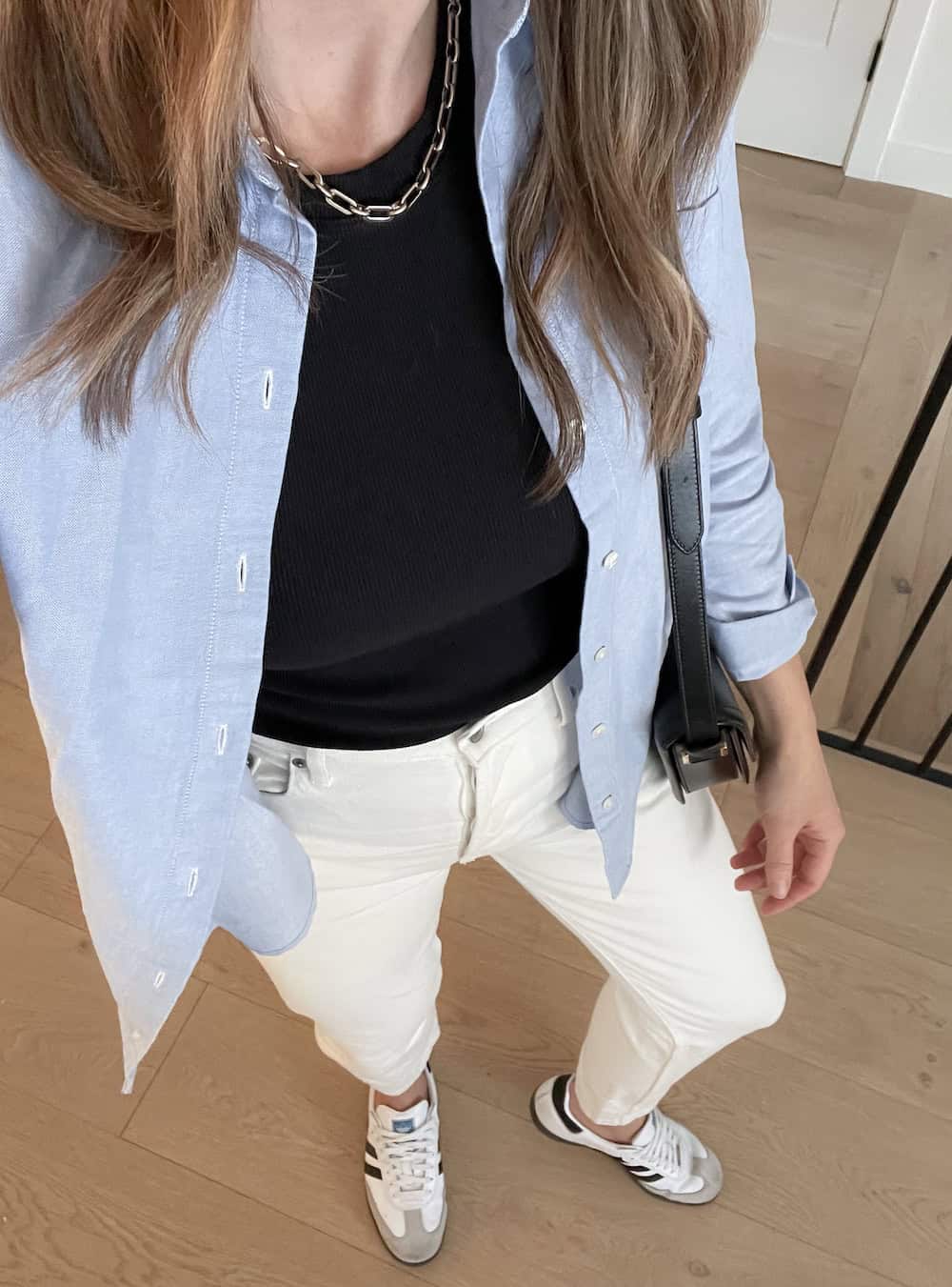 Christal wearing white jeans, a black t-shirt and an oversized blue button down with sneakers.