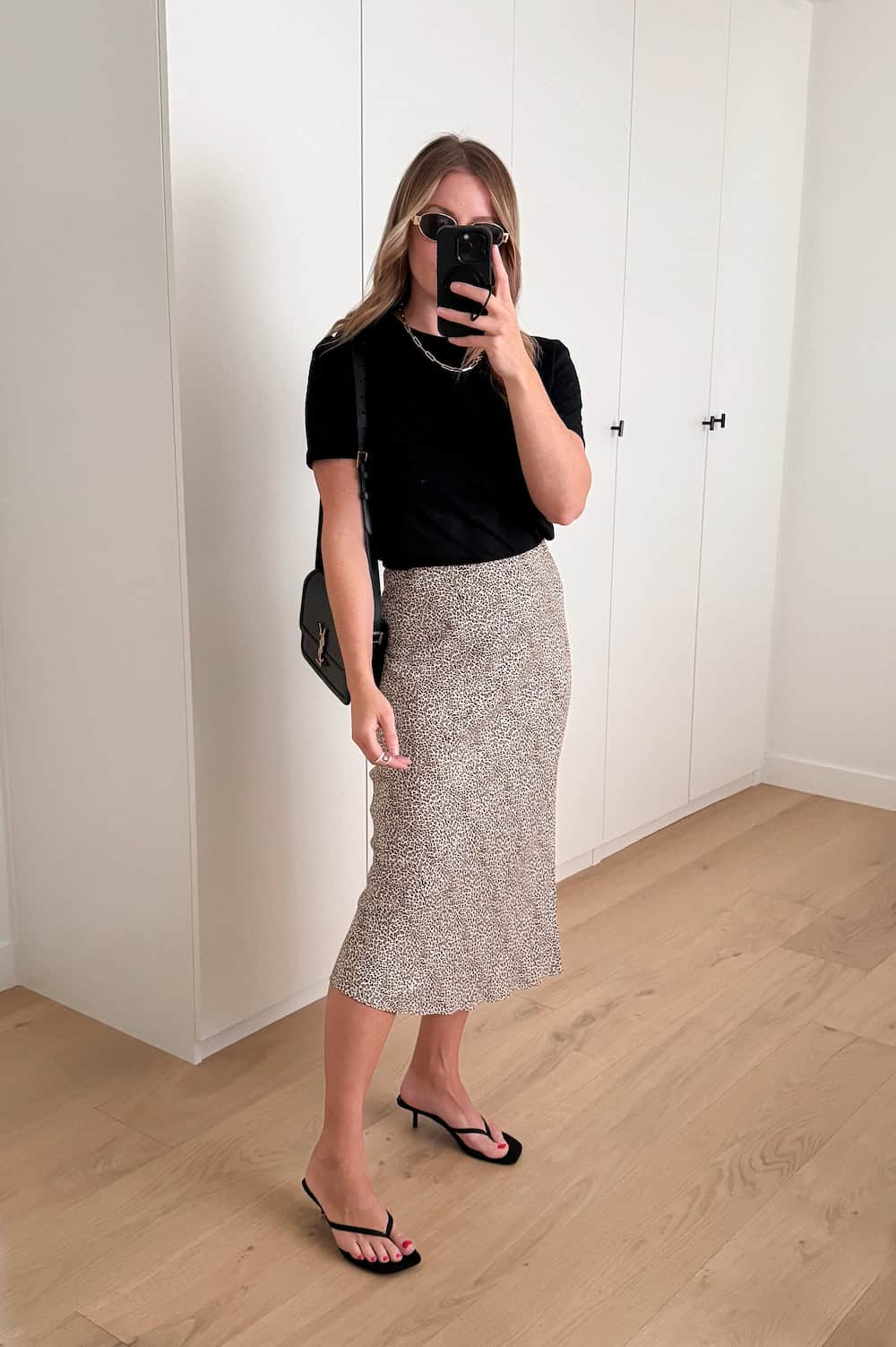 Woman wearing a printed slip skirt with a black t-shirt and black heeled sandals.