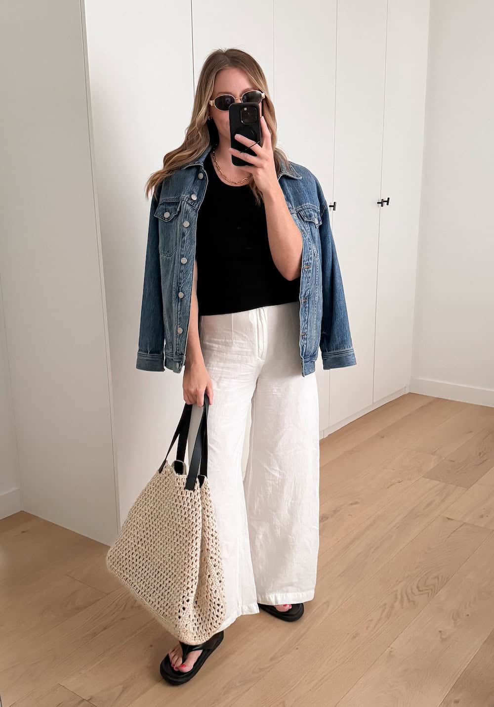 Christal wearing white, wide leg pants and a black tank top with a denim jacket.