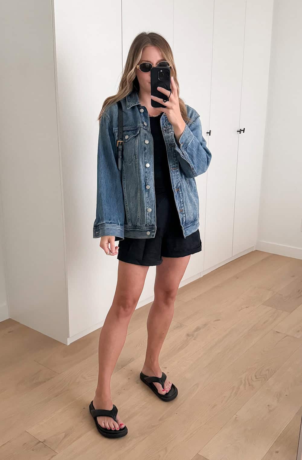 Christal wearing black shorts and a black tank top with a denim jacket and sandals.