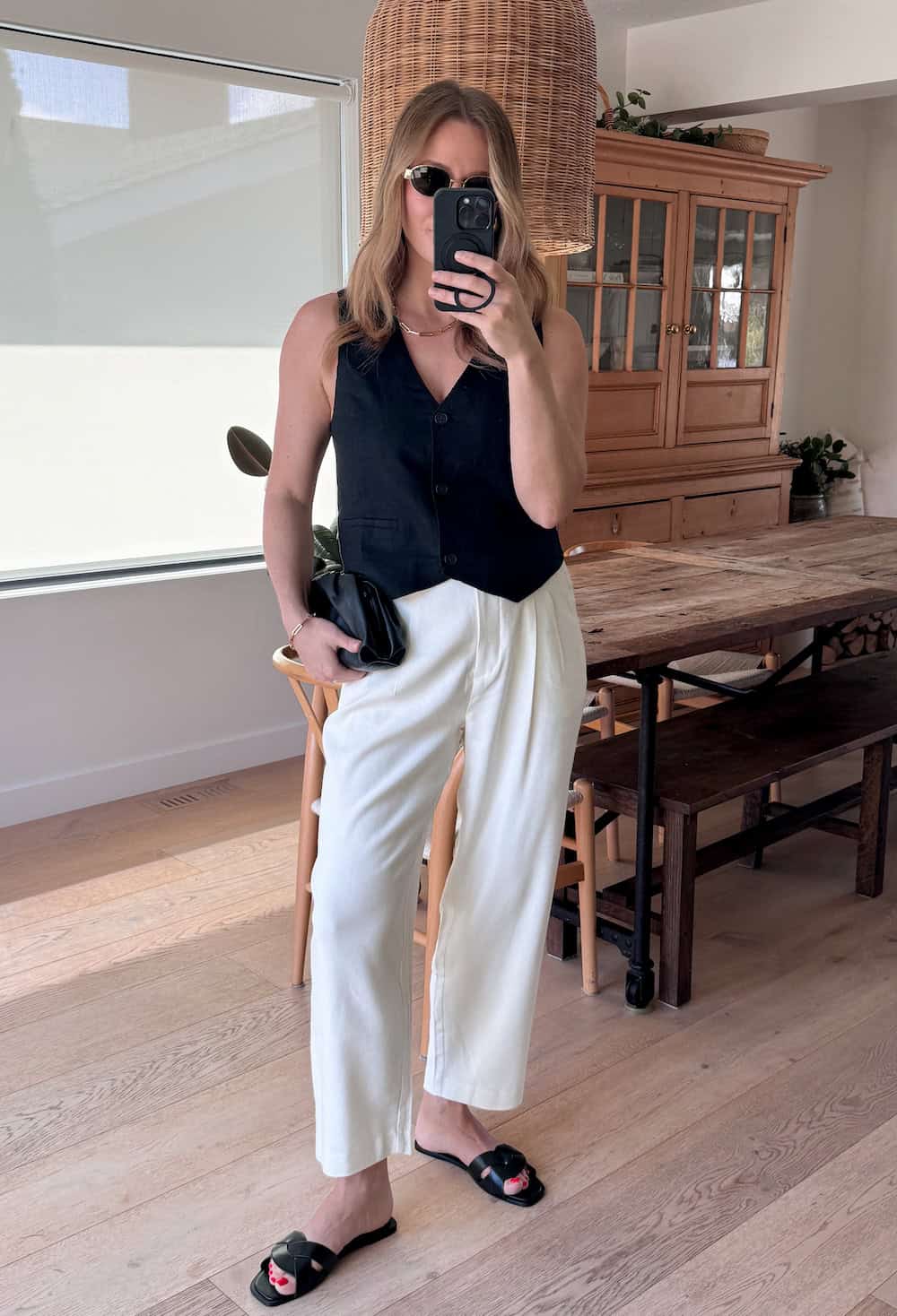 Christal wearing white tailored pants with a black vest top and black sandals.