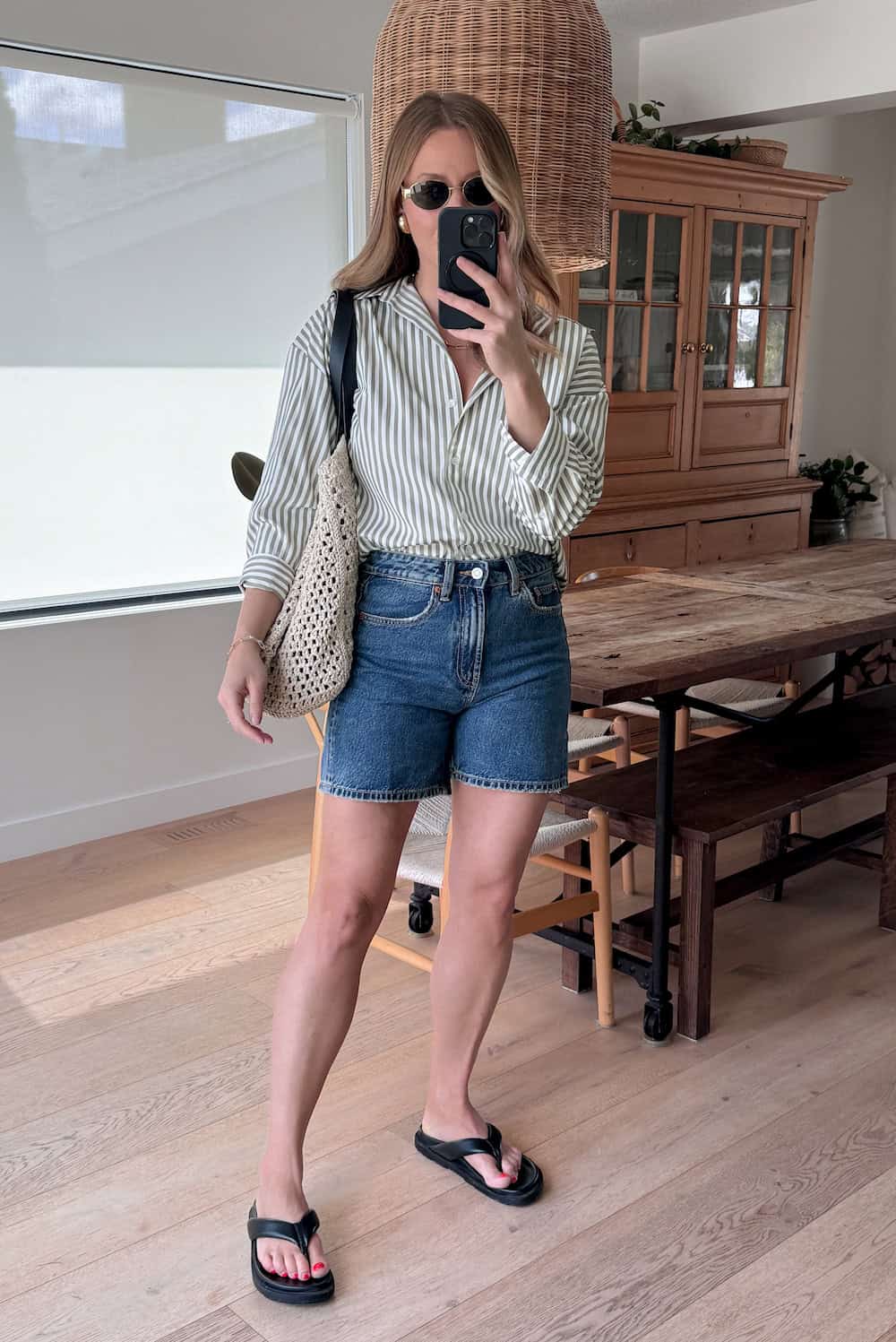 Christal wearing denim shorts with a green and white striped button down and sandals.
