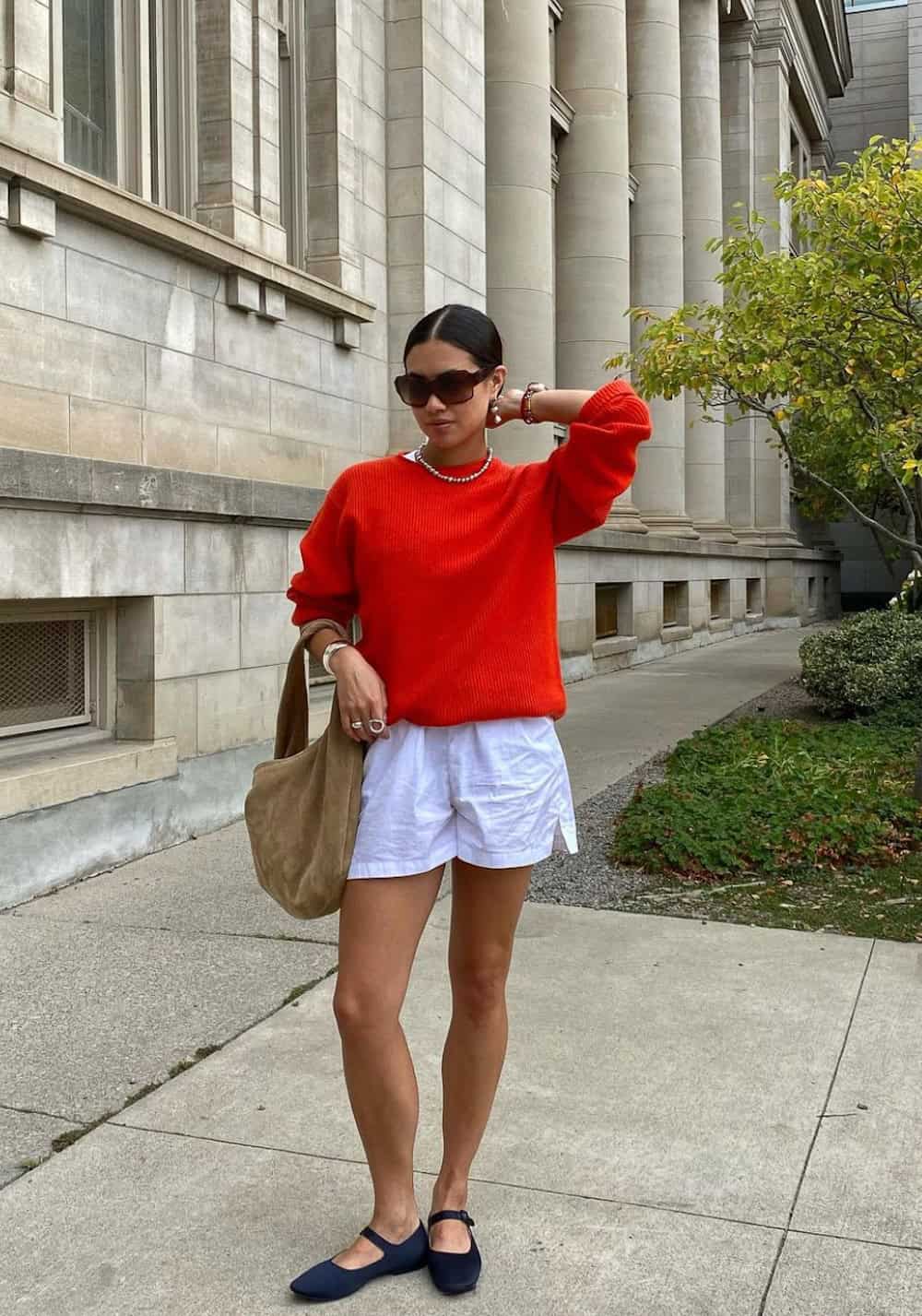 Woman wearing linen shorts with navy Mary Jane flats and a red sweater.