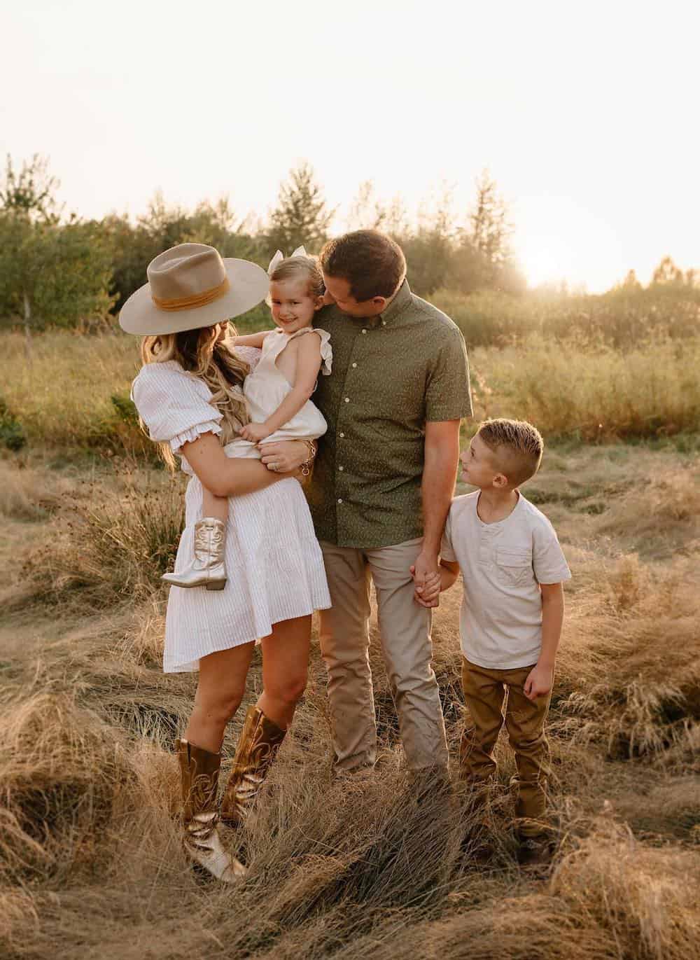 a fall family portrait where the mom is wearing a striped white mini dress, gold cowgirl boots, and a wide-brimmed hat while the rest of the family is dressed in neutrals with pops of warm fall colors