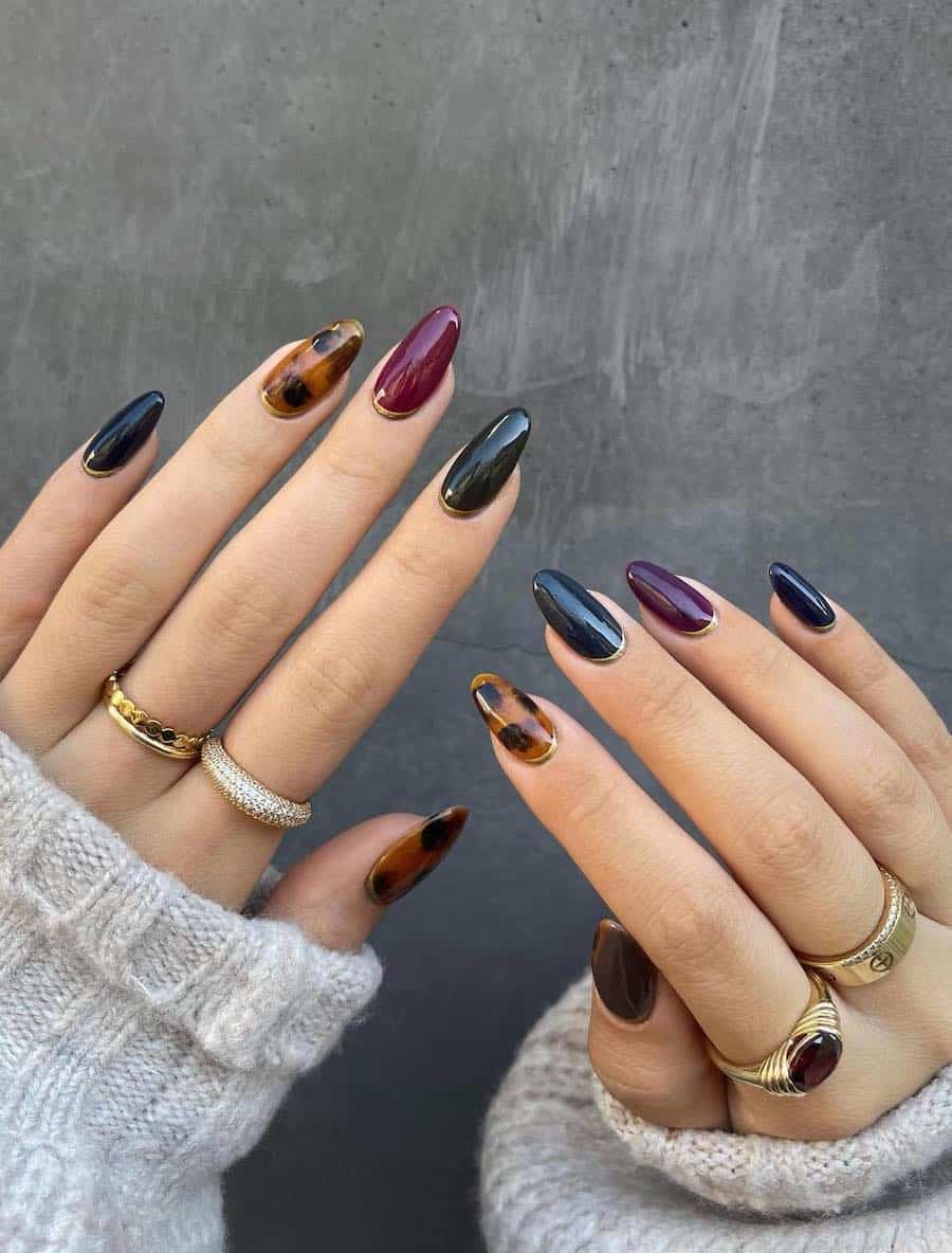 short almond nails with gradient fall colors, tortoise shell accent nails, and gold reverse French tips