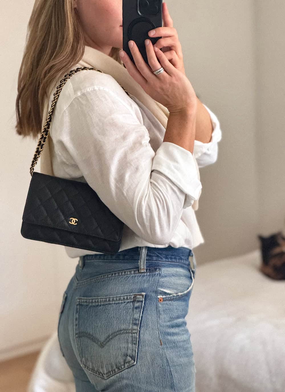 Woman wearing a black Chanel wallet on chain wearing a white button up shirt, cream sweater, and blue jeans