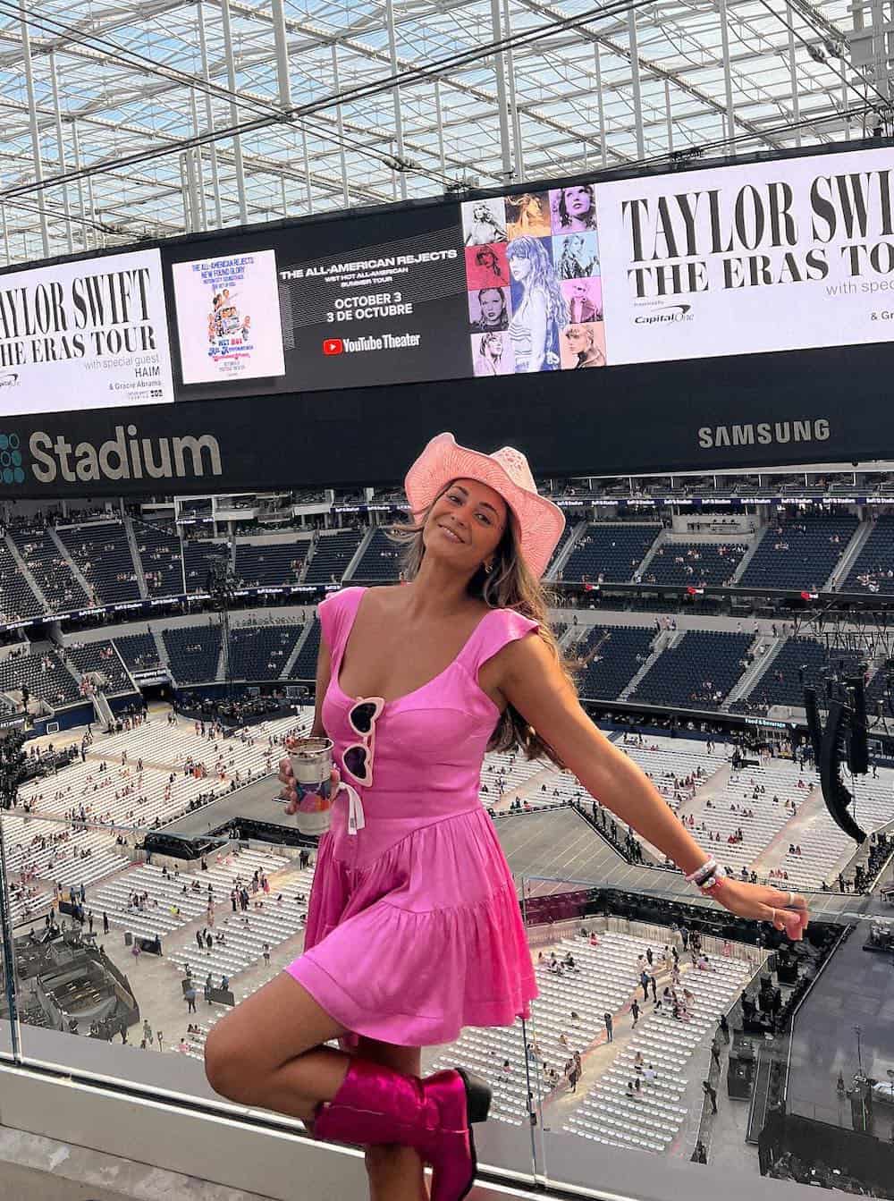 a woman wearing a summer concert outfit featuring a pink mini dress metallic pink cowboy boots, and a pink cowgirl hat