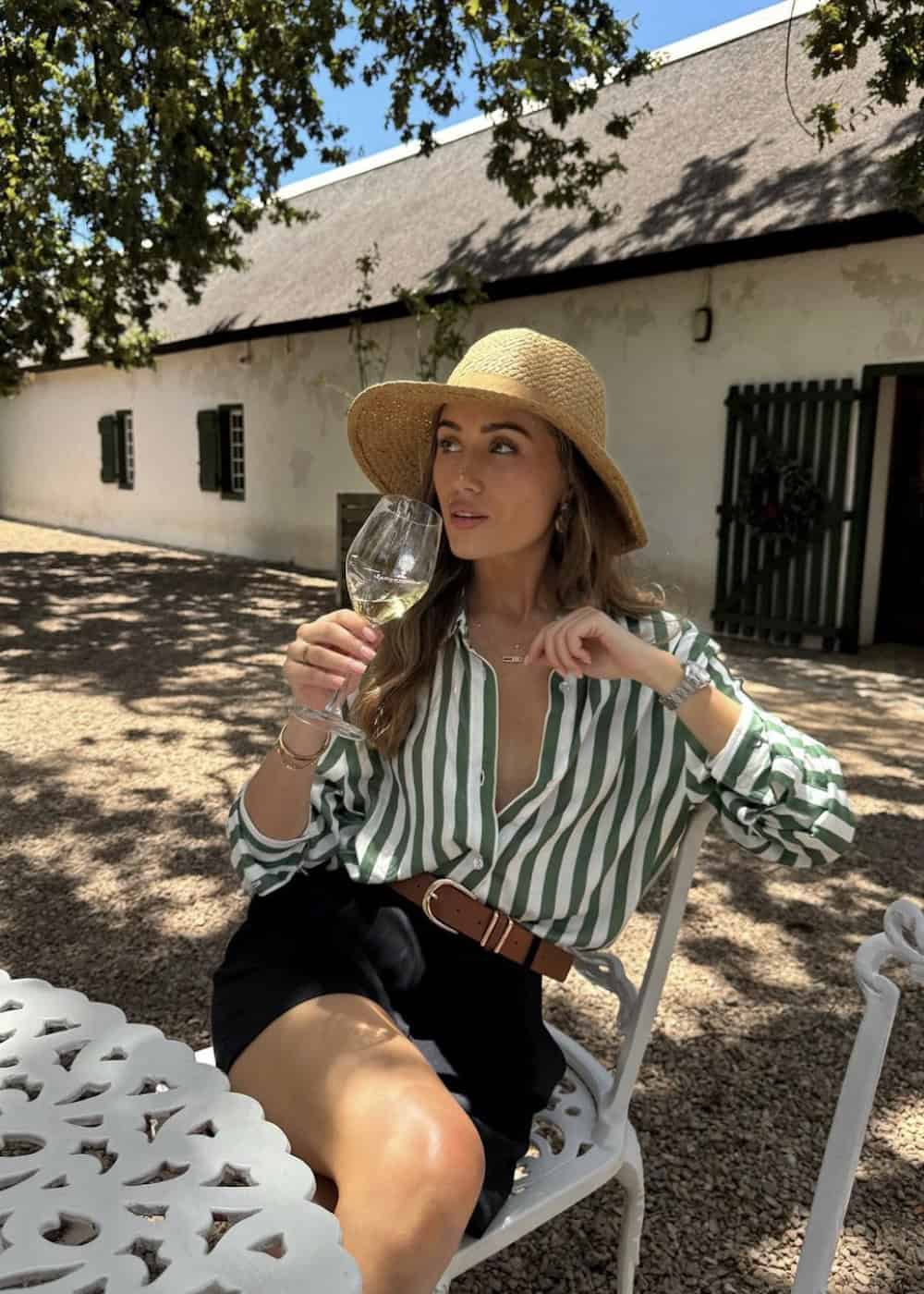 Woman wearing black shorts with a striped button down and a straw hat.