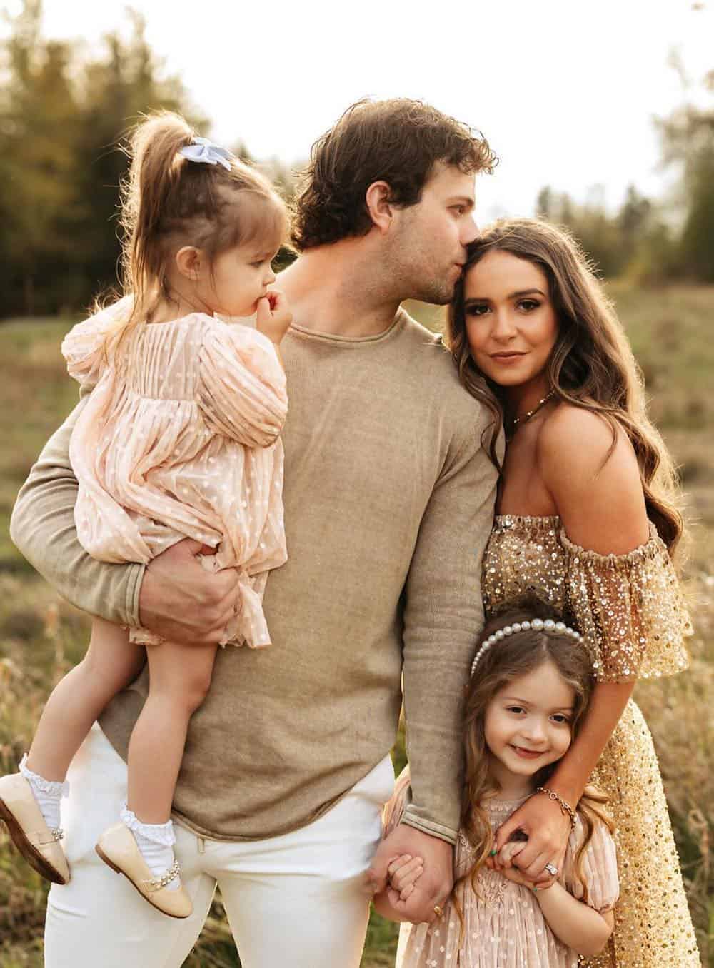 a summer family photo shoot where to mom is wearing an off-the-shoulder dress with gold accents while the dad wears neutral pieces and the daughters wear neutral polka dot dresses