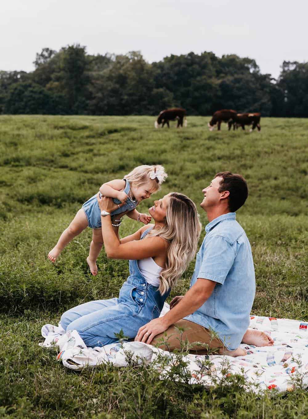 a summer family photo shoot with a mom, dad, and baby girl wearing casual denim pieces like overalls, rompers, and shirts
