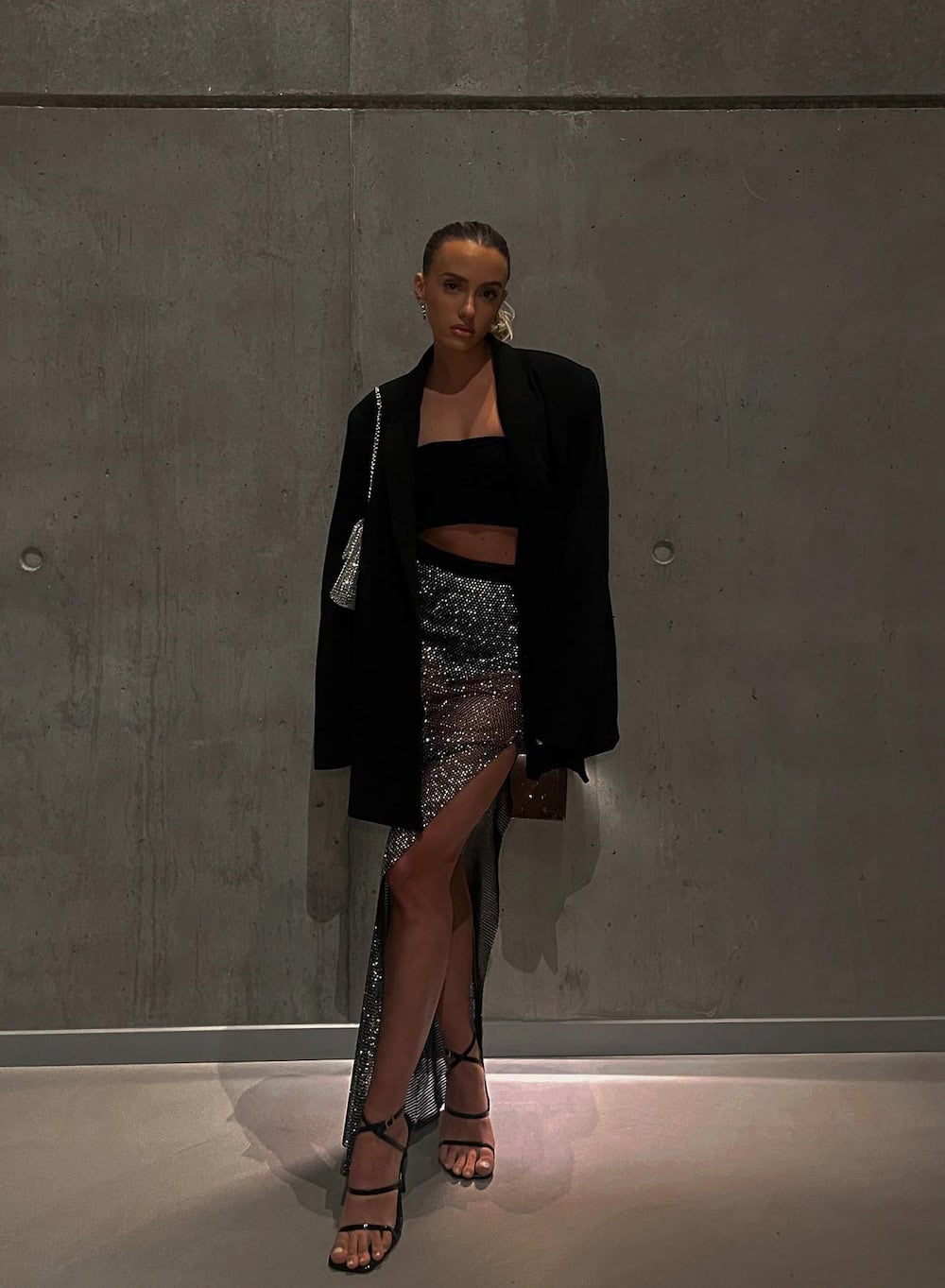 a woman wearing a slitted silver gem embellished maxi skirt, a black crop top, a black blazer, and black strappy heels