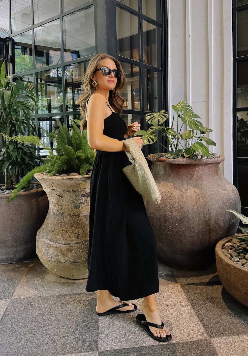 a woman wearing a black maxi dress with sandals and a woven tote