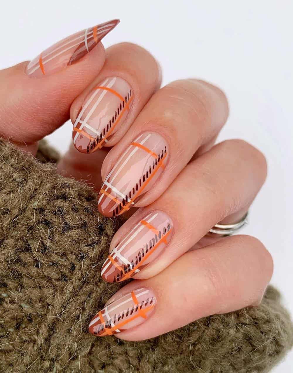 long nude almond nails with a plaid design over burnt orange tips