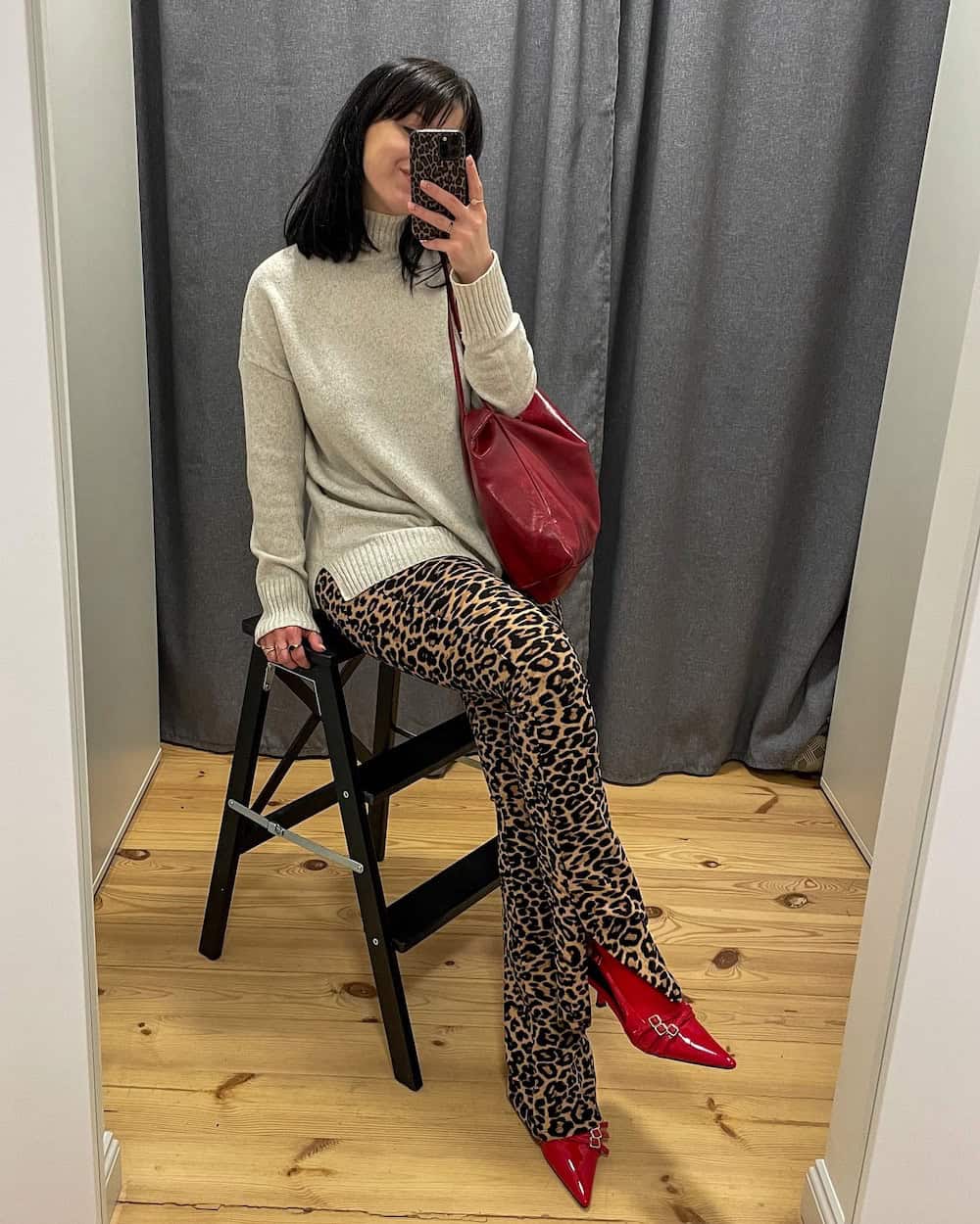 Woman wearing leopard print pants with a grey sweater and red pumps.