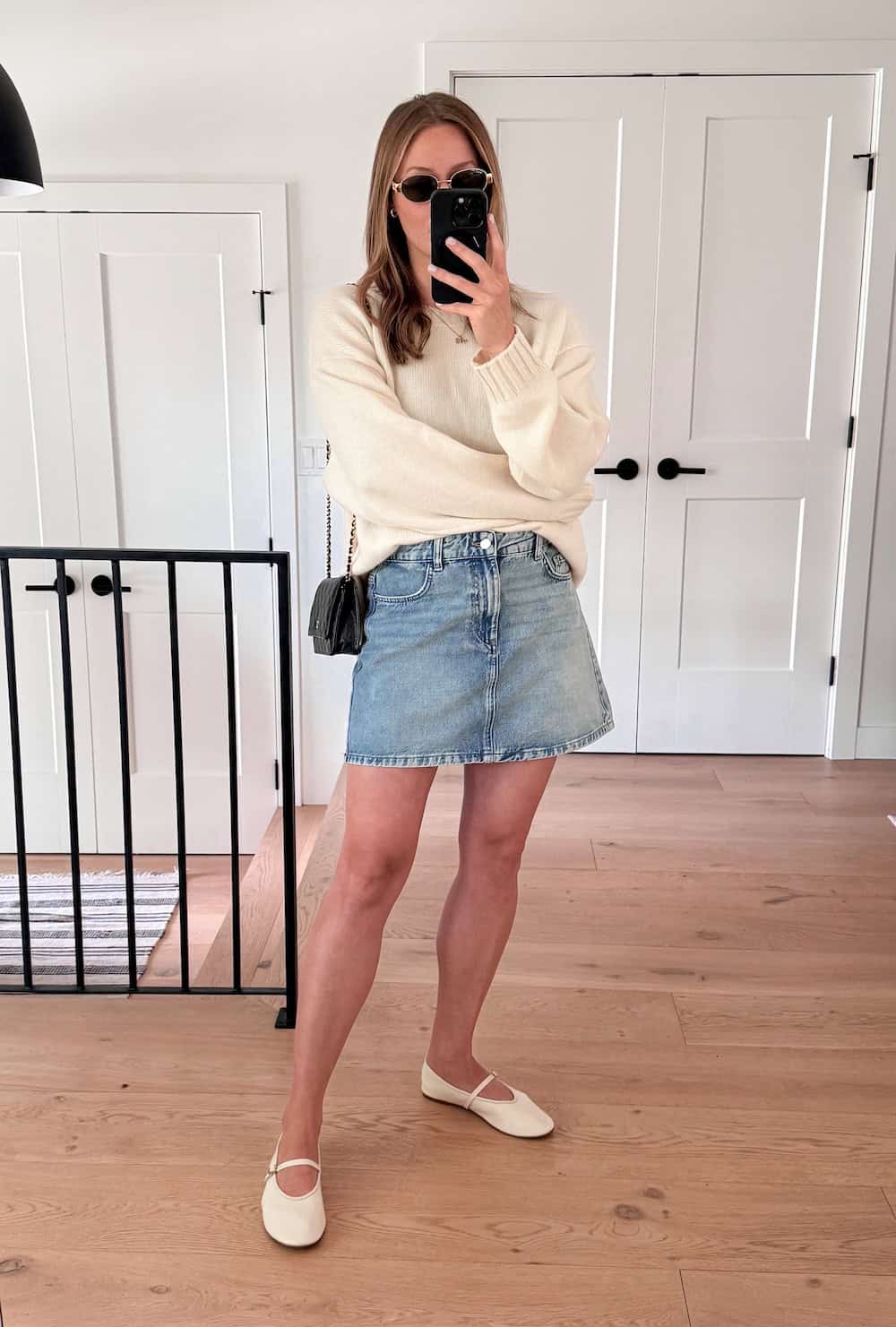 Christal wearing a denim skirt with a cream sweater and cream mary jane flats.