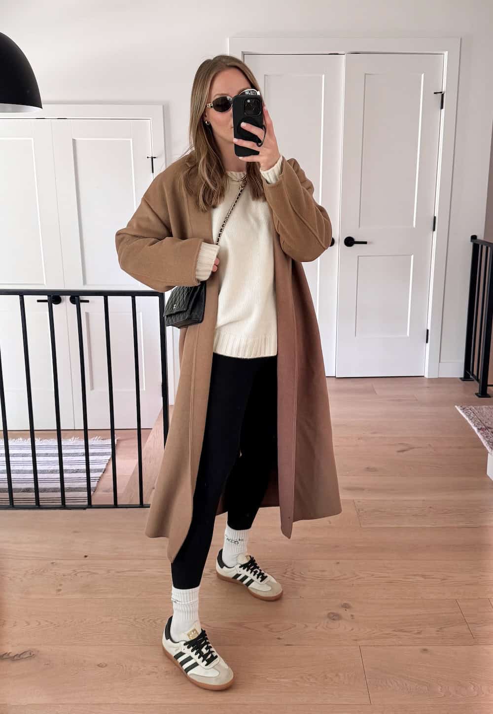 Christal wearing leggings with a white sweater and a long, camel colored coat with tall white socks and sneakers.
