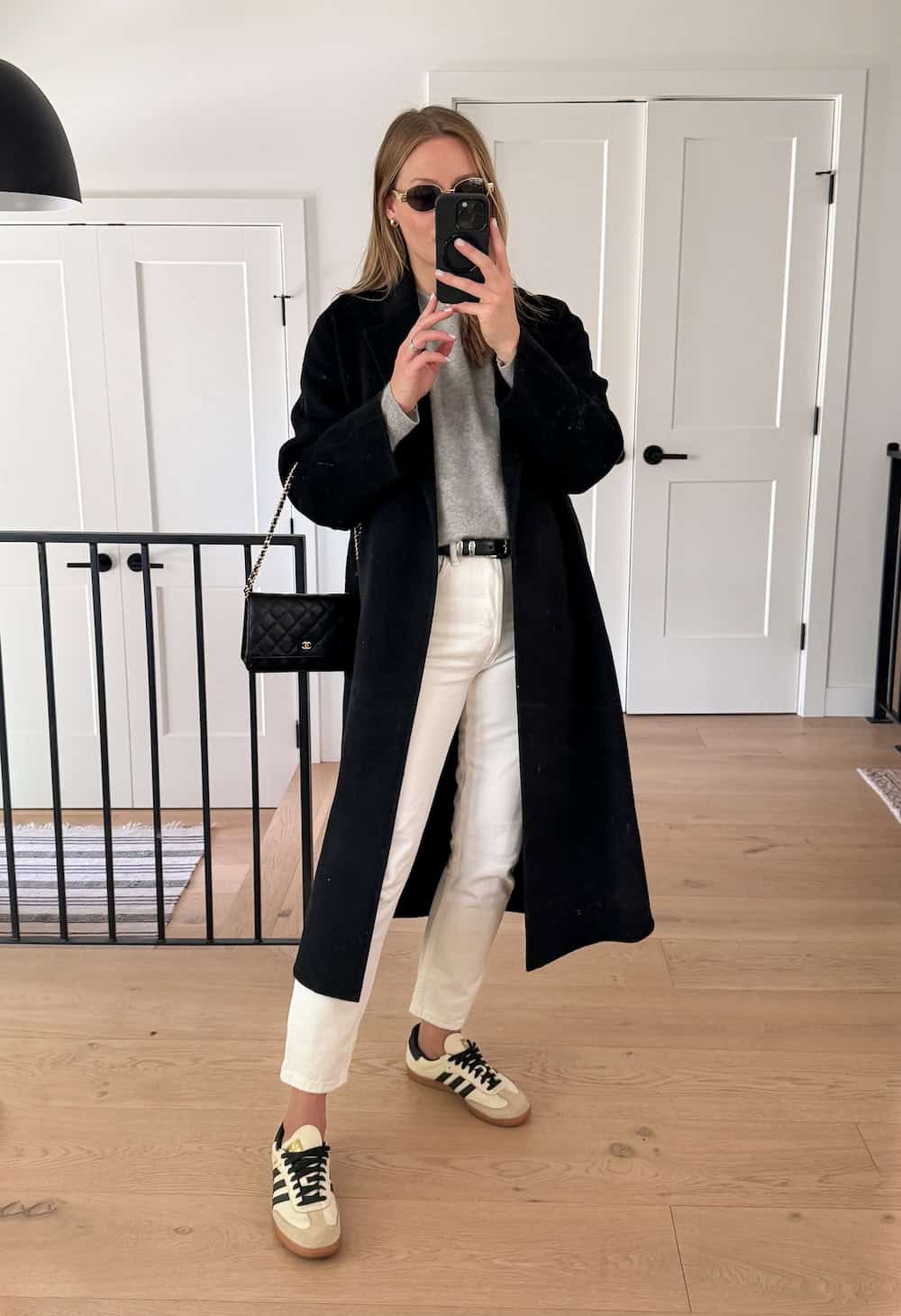 Christal wearing white jeans, a grey sweater, a long black coat and sneakers.