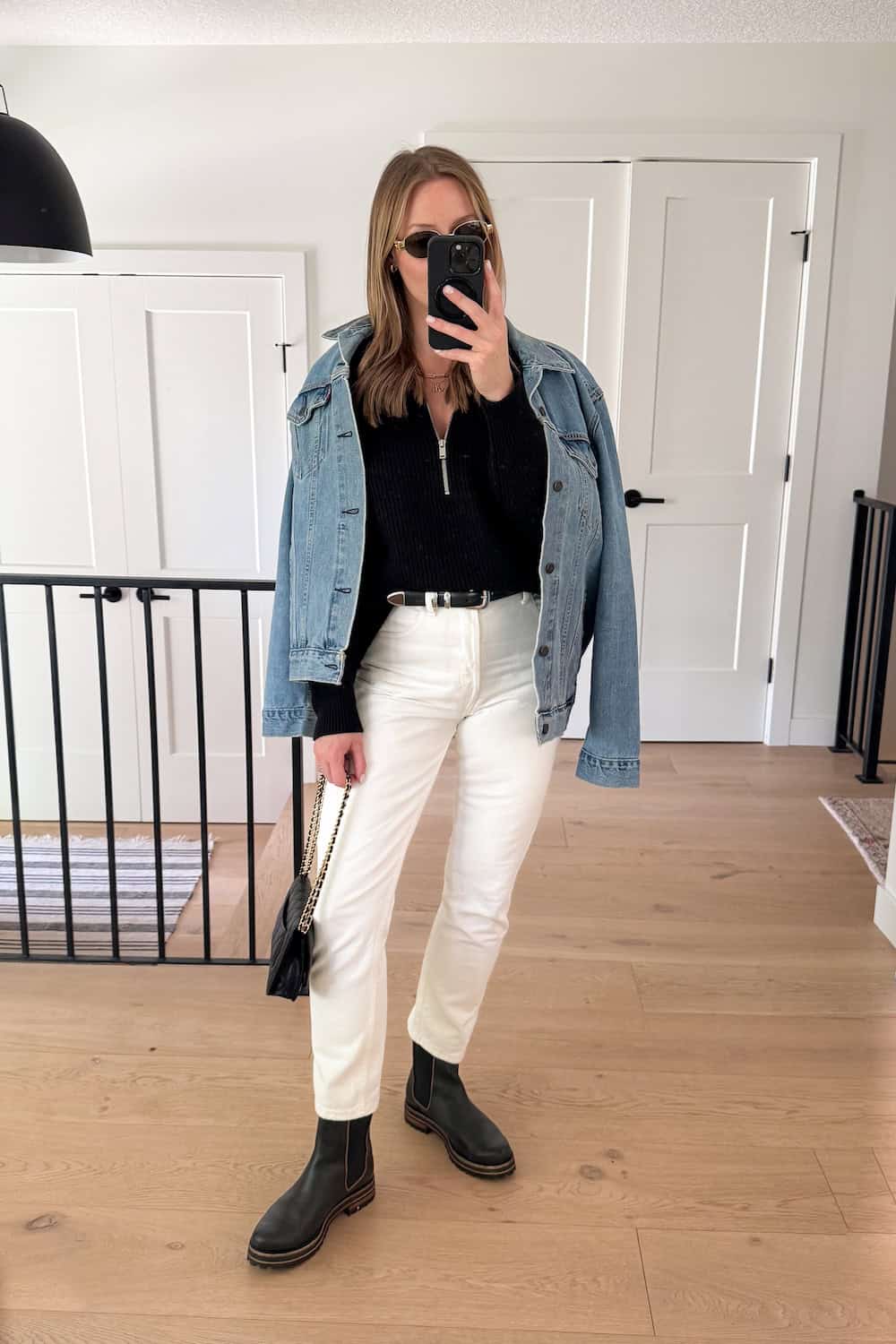Christal wearing white jeans, black boots, a black quarter zip sweater and a denim jacket over her shoulders.