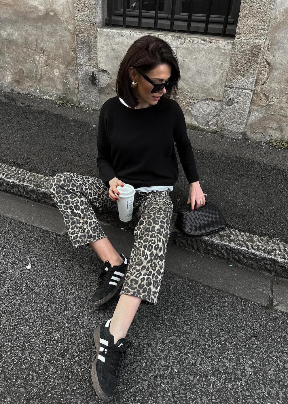 Woman wearing leopard print jeans, a black sweater over a white button down and black sneakers.