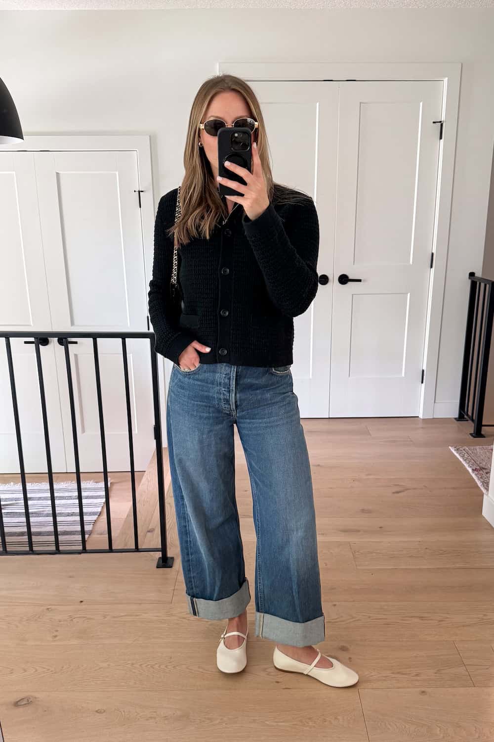 Christal wearing wide-leg jeans with cream mary jane flats and a black cardigan.