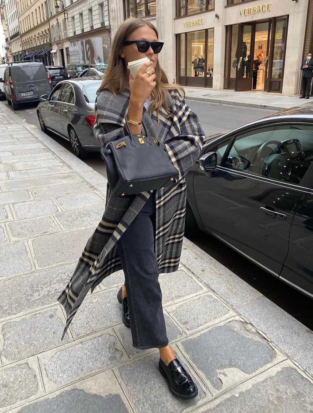Woman wearing dark jeans, a plaid coat and Prada loafers with black accessories.