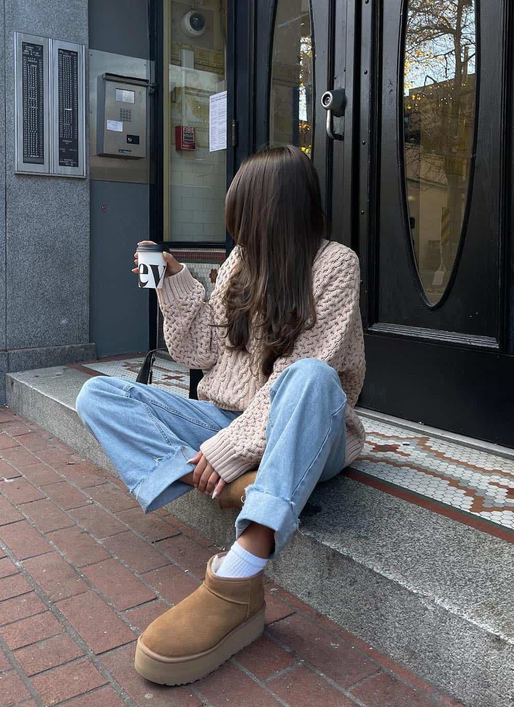 Woman wearing jeans with a a chunky neutral sweater and platform Ugg boots.