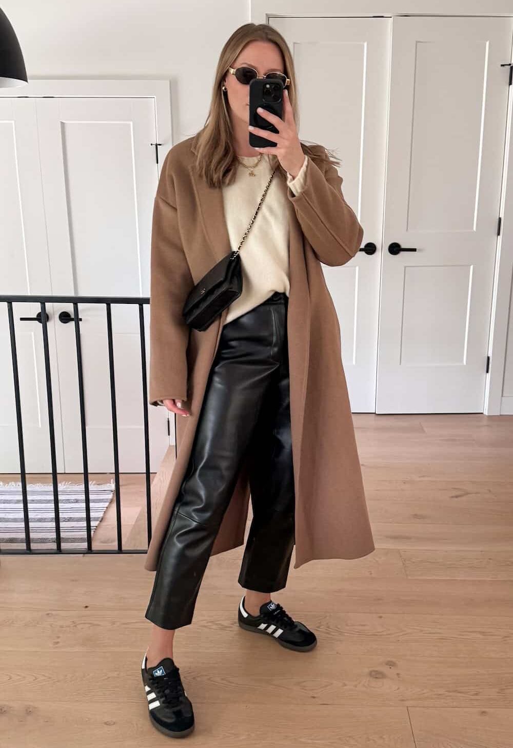 Christal wearing black leather pants, black sneakers, a white sweater and a tan trench coat.