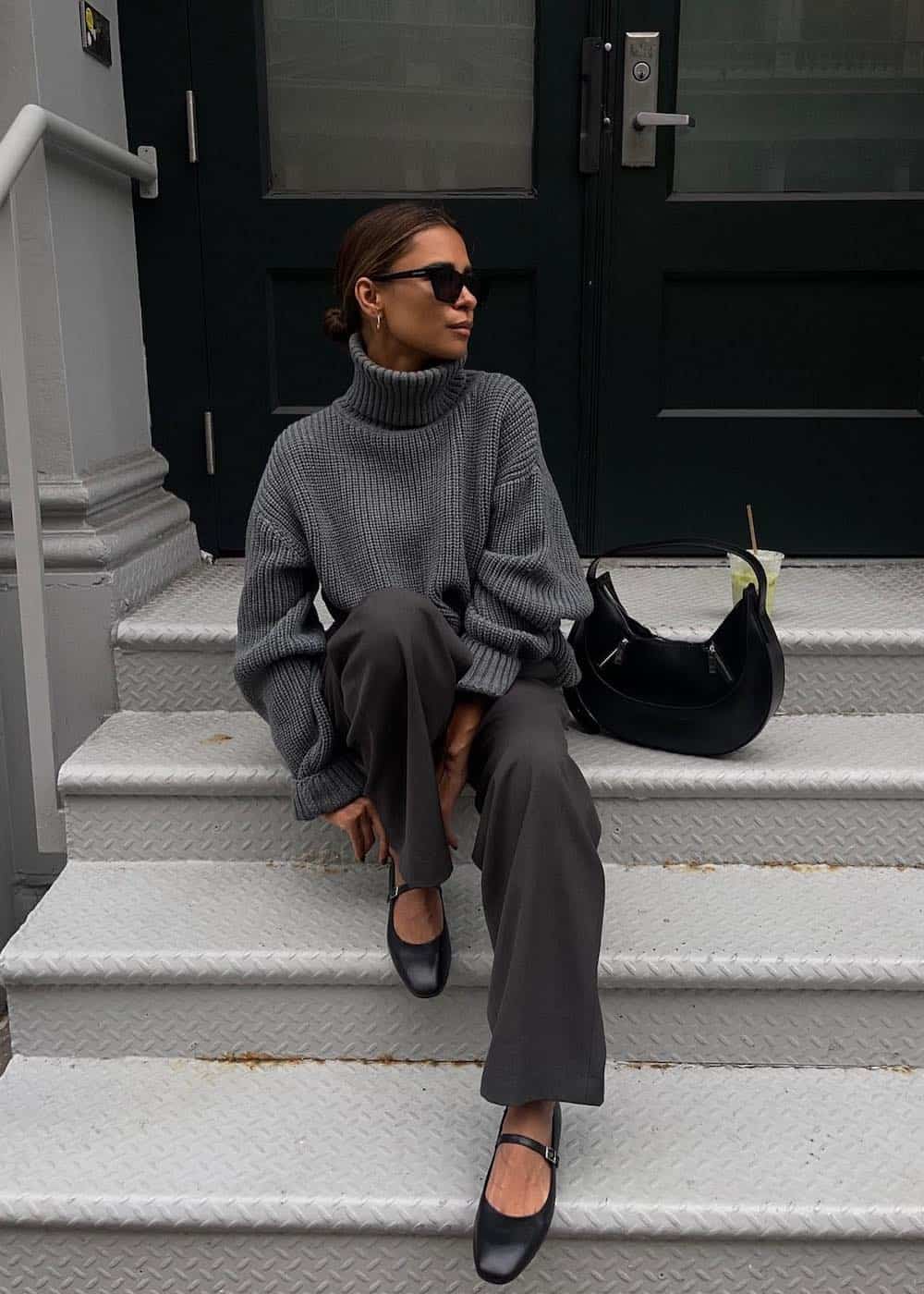 Woman wearing grey trousers with a grey turtle neck sweater and black mary jane flats.