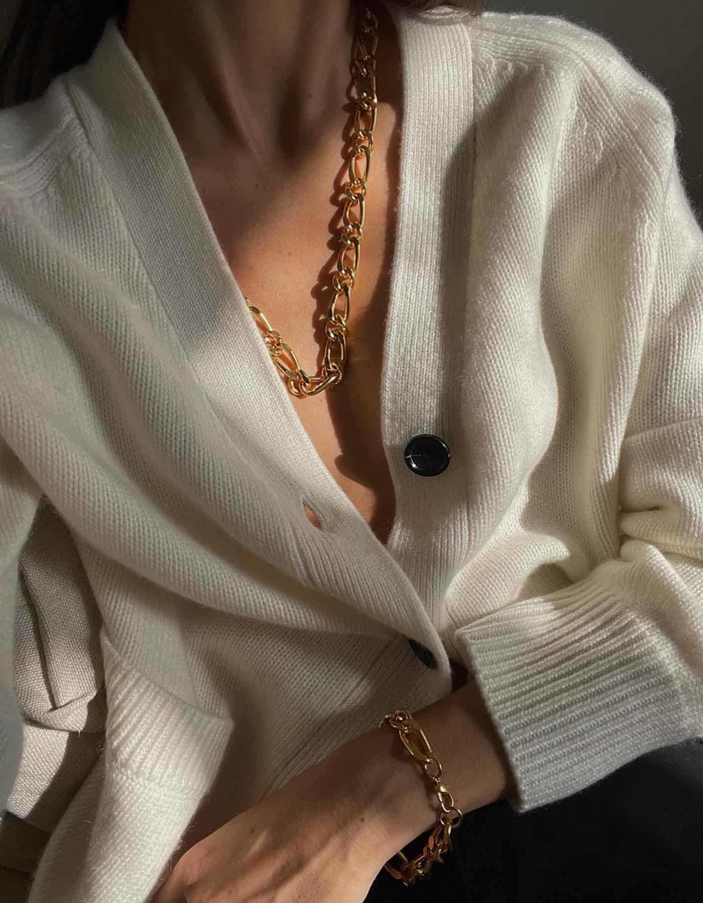 Close up image of a woman wearing a white cardigan with gold jewelry.