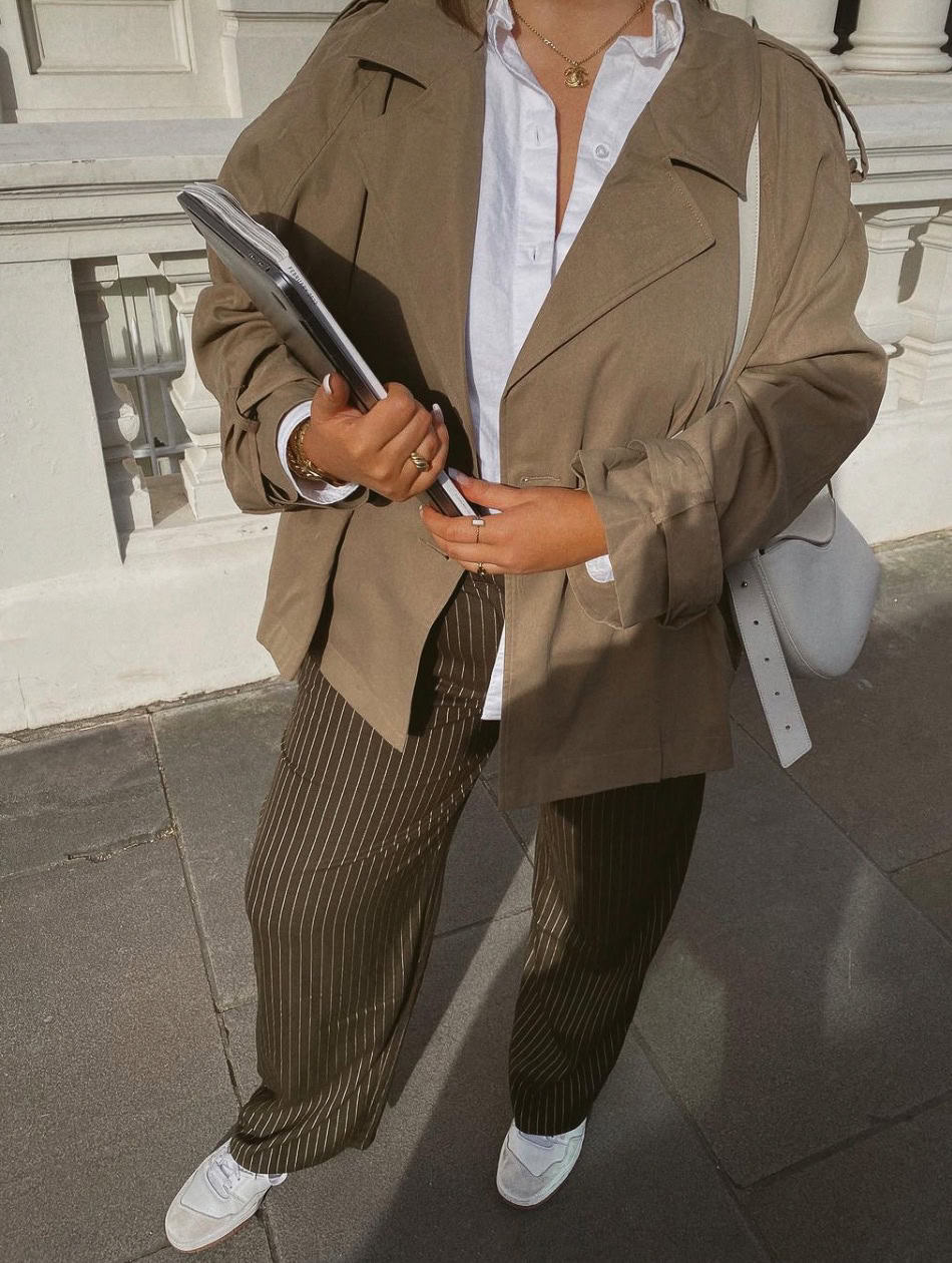 Woman wearing brown and white pin stripe trousers with a white button down and an oversized blazer jacket.