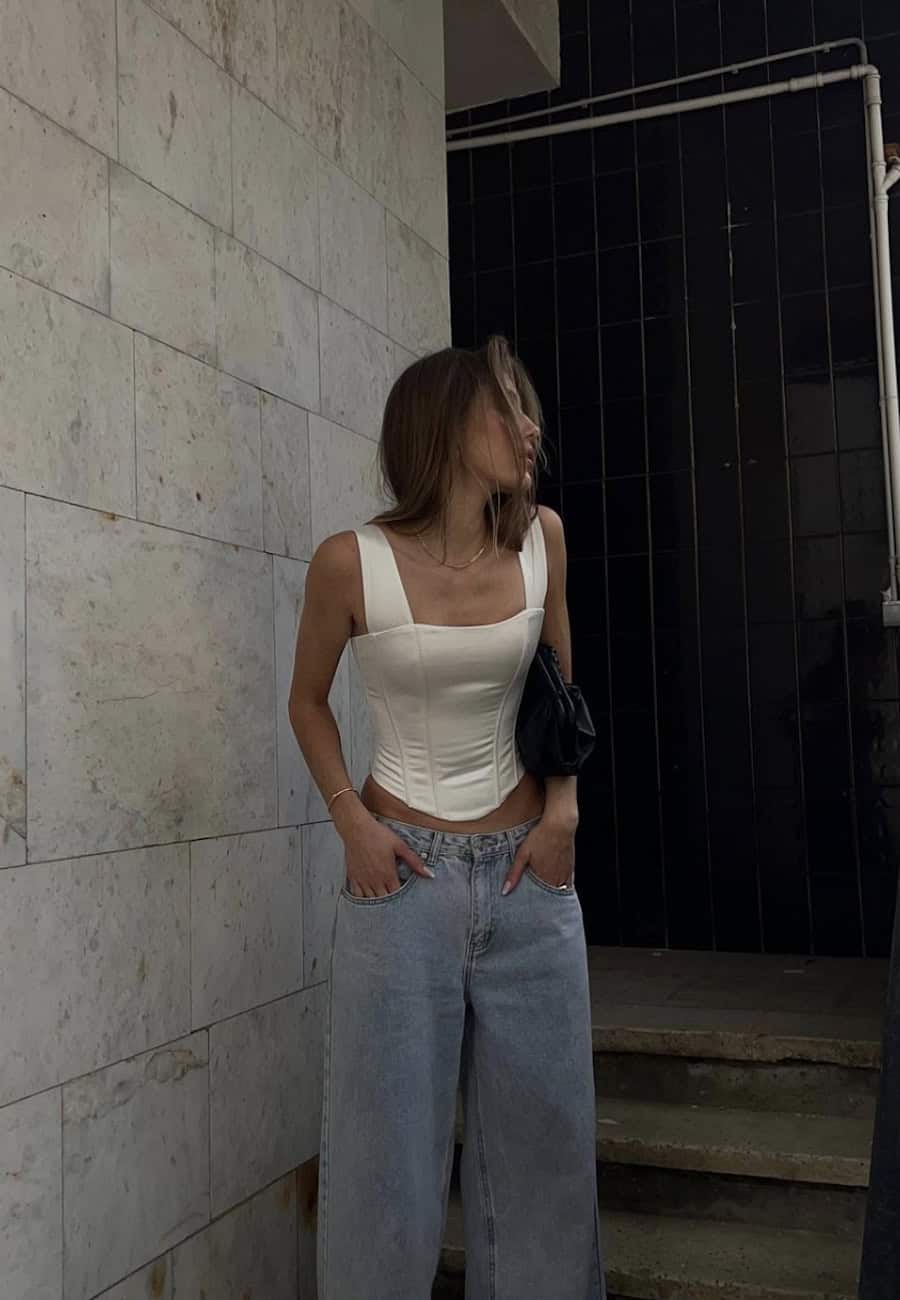 Woman wearing baggy jeans with a white silk corset top.