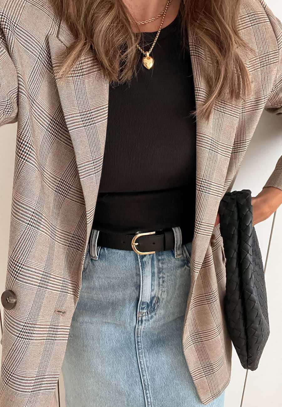 Christal wearing denim, a black knot top and a plaid blazer with gold jewelry.