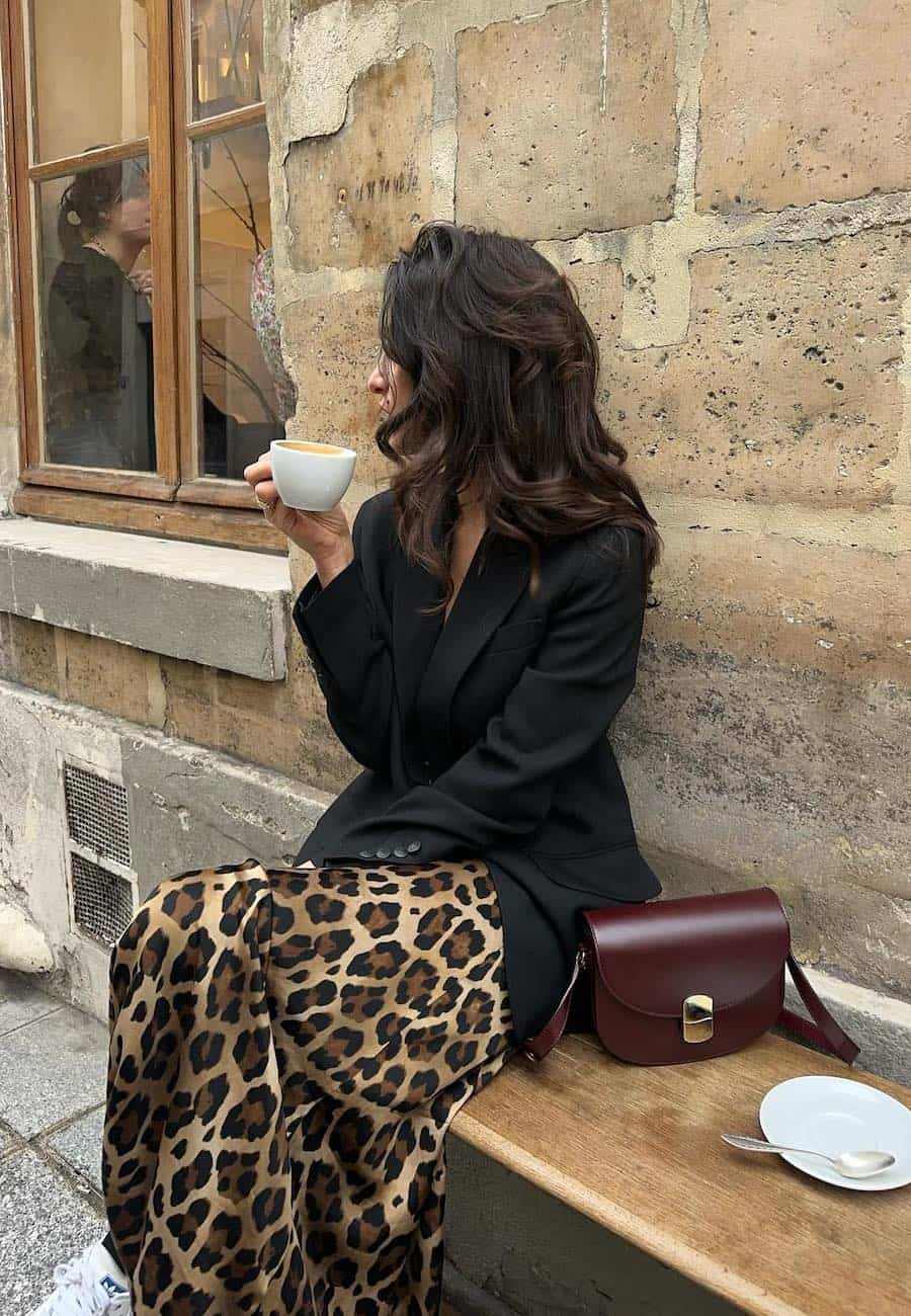 Woman wearing a leopard print midi skirt with sneakers and a black blazer.