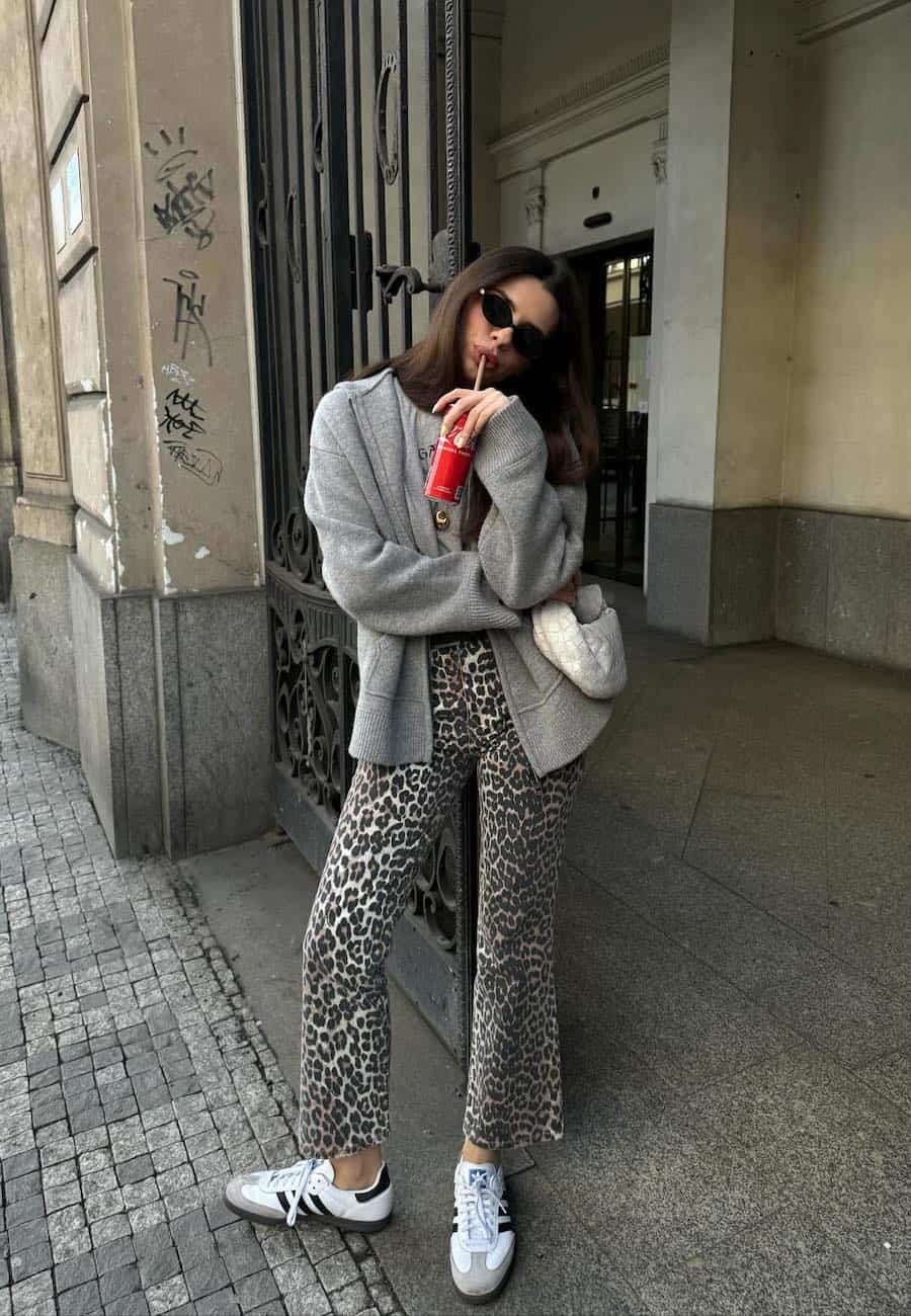 Woman wearing leopard print jeans with sneakers, a graphic tee and a cardigan.