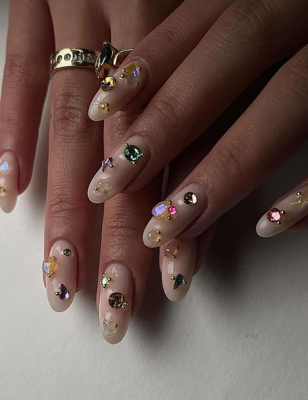 long round nude nails with gems, pearls, and gold charms