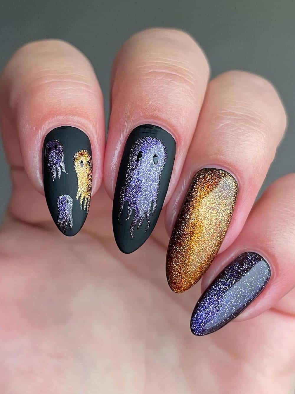 long glittering gold and purple polish on black almond nails featuring ghost nail art