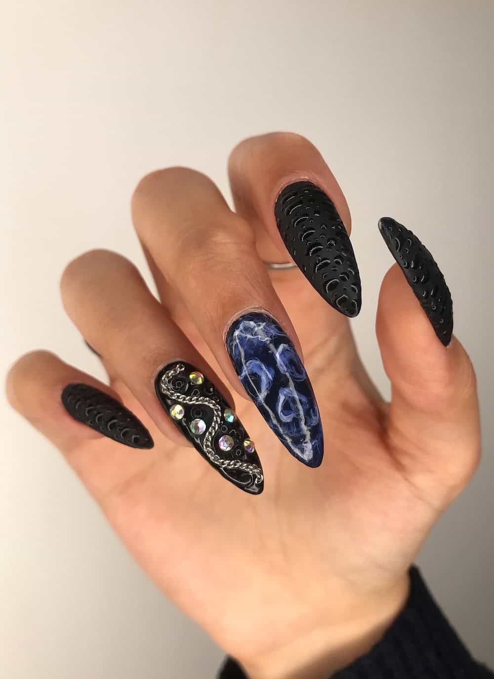 long black almond nails with a skeleton face accent nails, shiny 3D dots, and chain and gem details