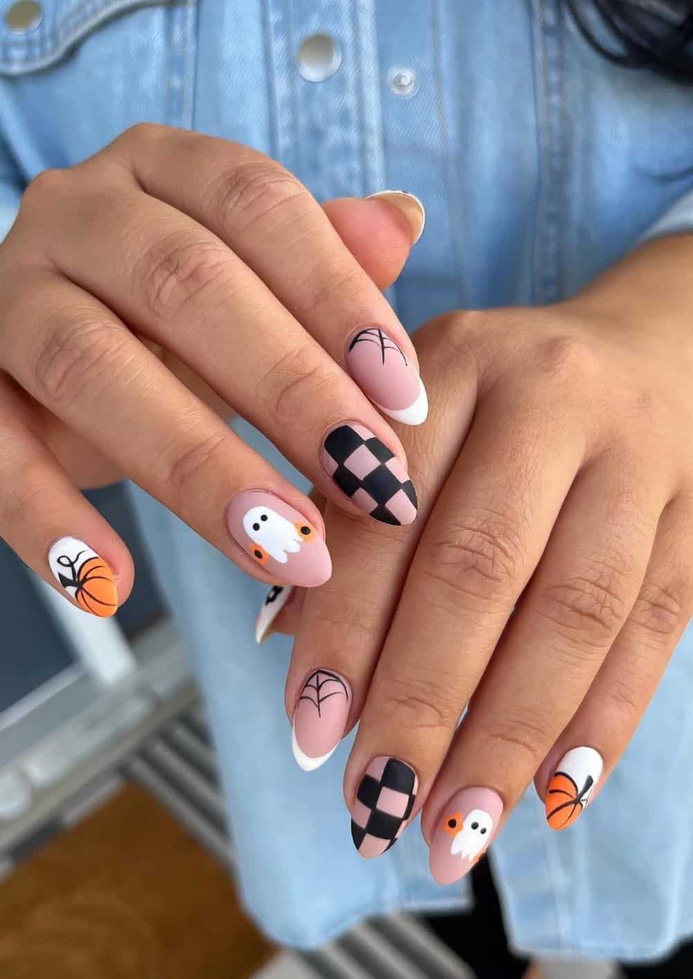 medium nude pink almond nails with pumpkin tips, ghost art, spider webs, and checkerboard details