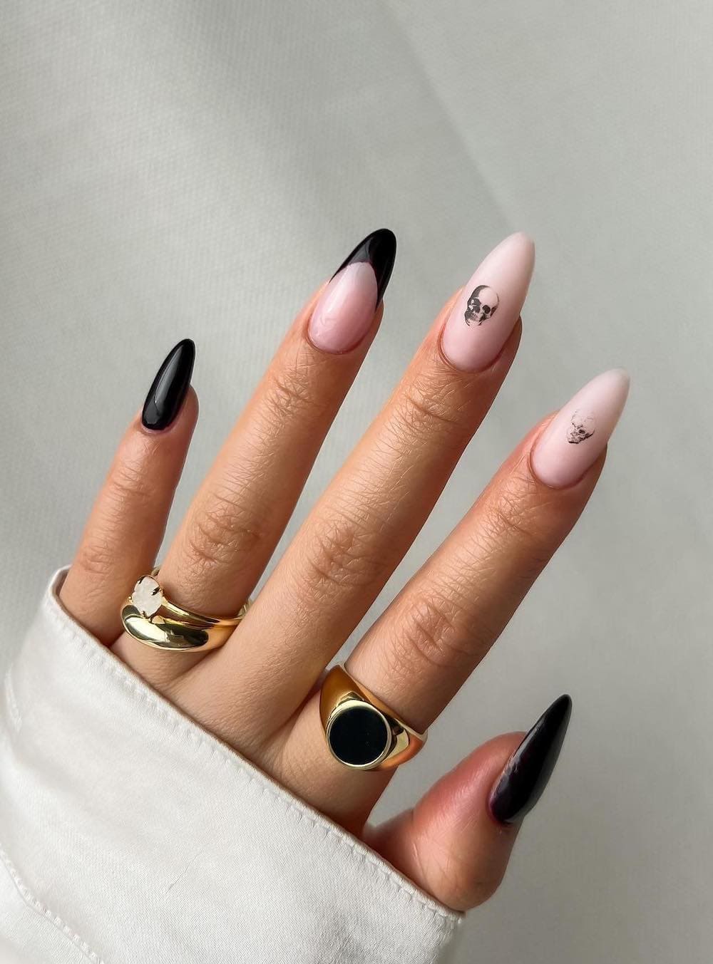 long nude almond nails with black accent nails, black tips, and skull nail stickers