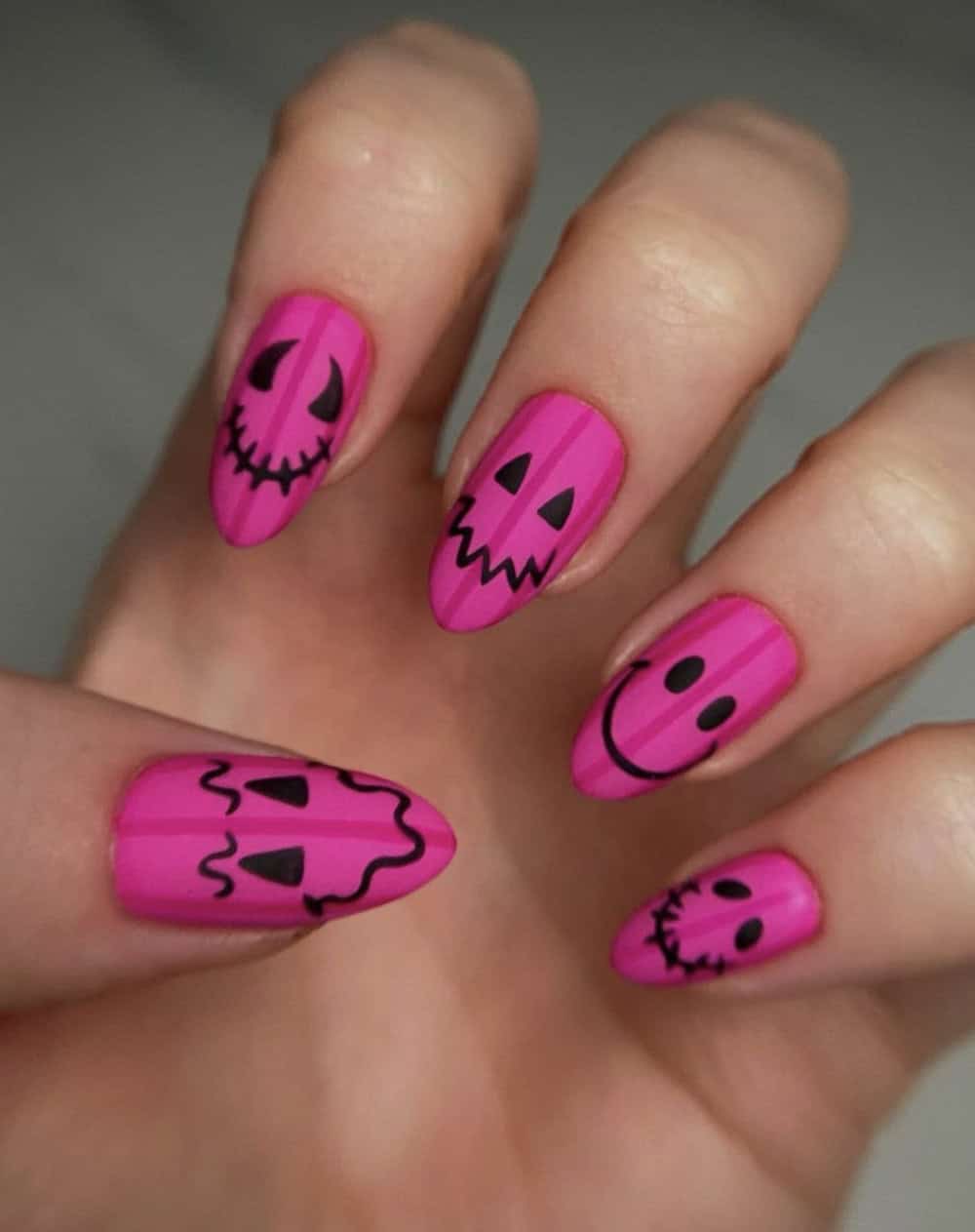 long matte pink almond nails with dark pink stripes and black pumpkin faces