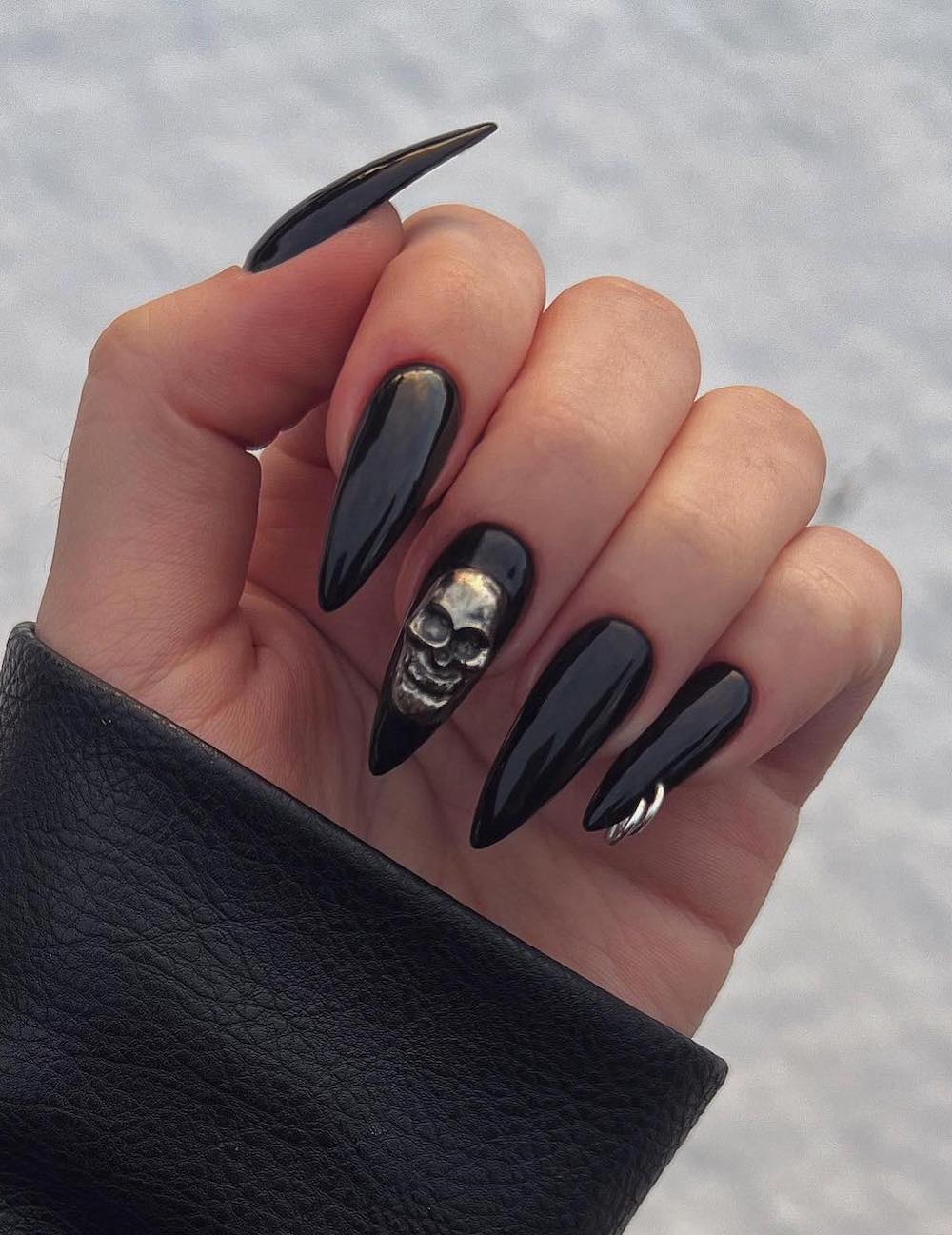 long black stiletto nails with a 3D skull and nail piercings