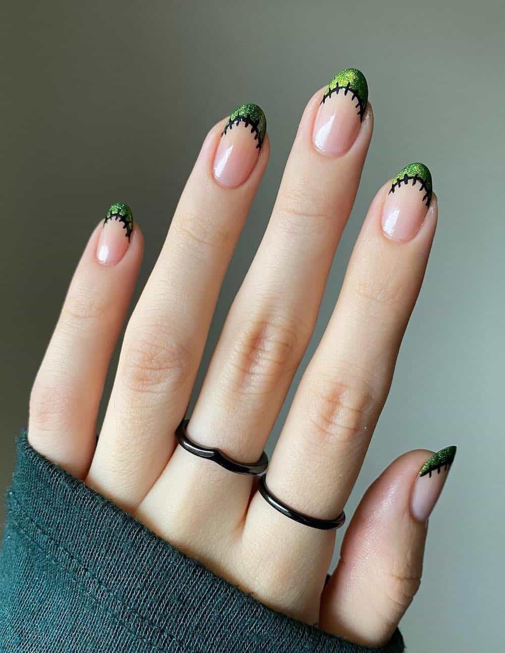 short nude almond nails with shimmering green tips and black stitched borders