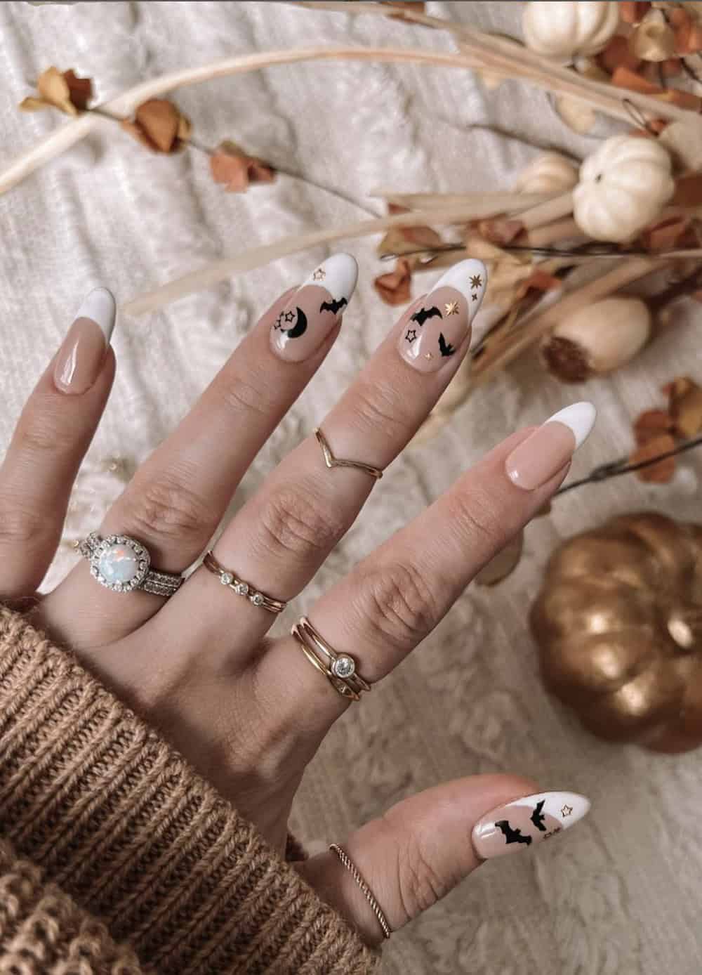 long nude almond nails with white tips, gold star details, and black bats and moons