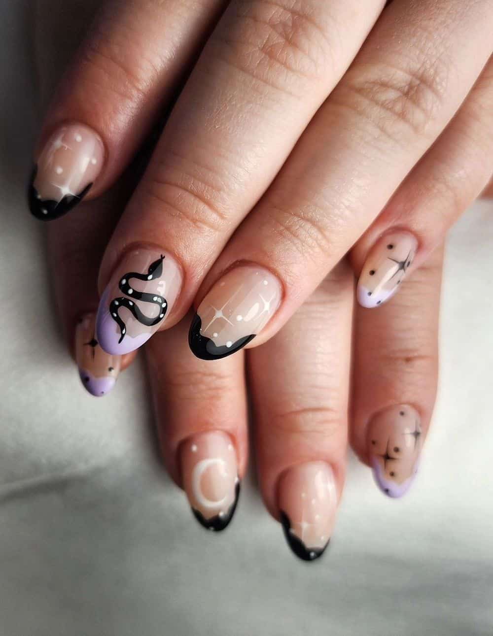 short nude almond nails with wavy pastel purple and black tips, featuring stars, moons, and snake nail art