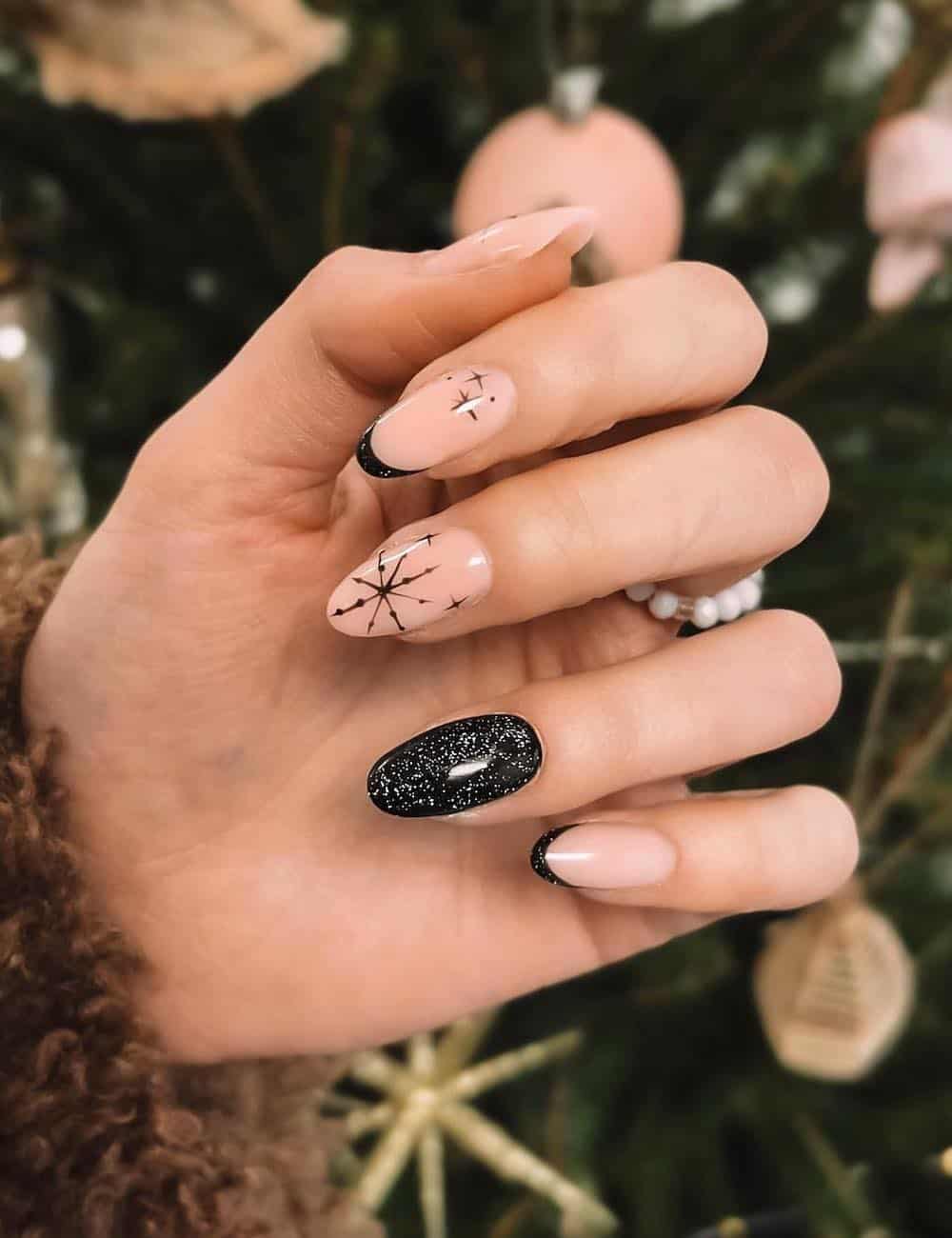 long nude almond nails with black designs like tips, snowflakes, and glitter topcoats